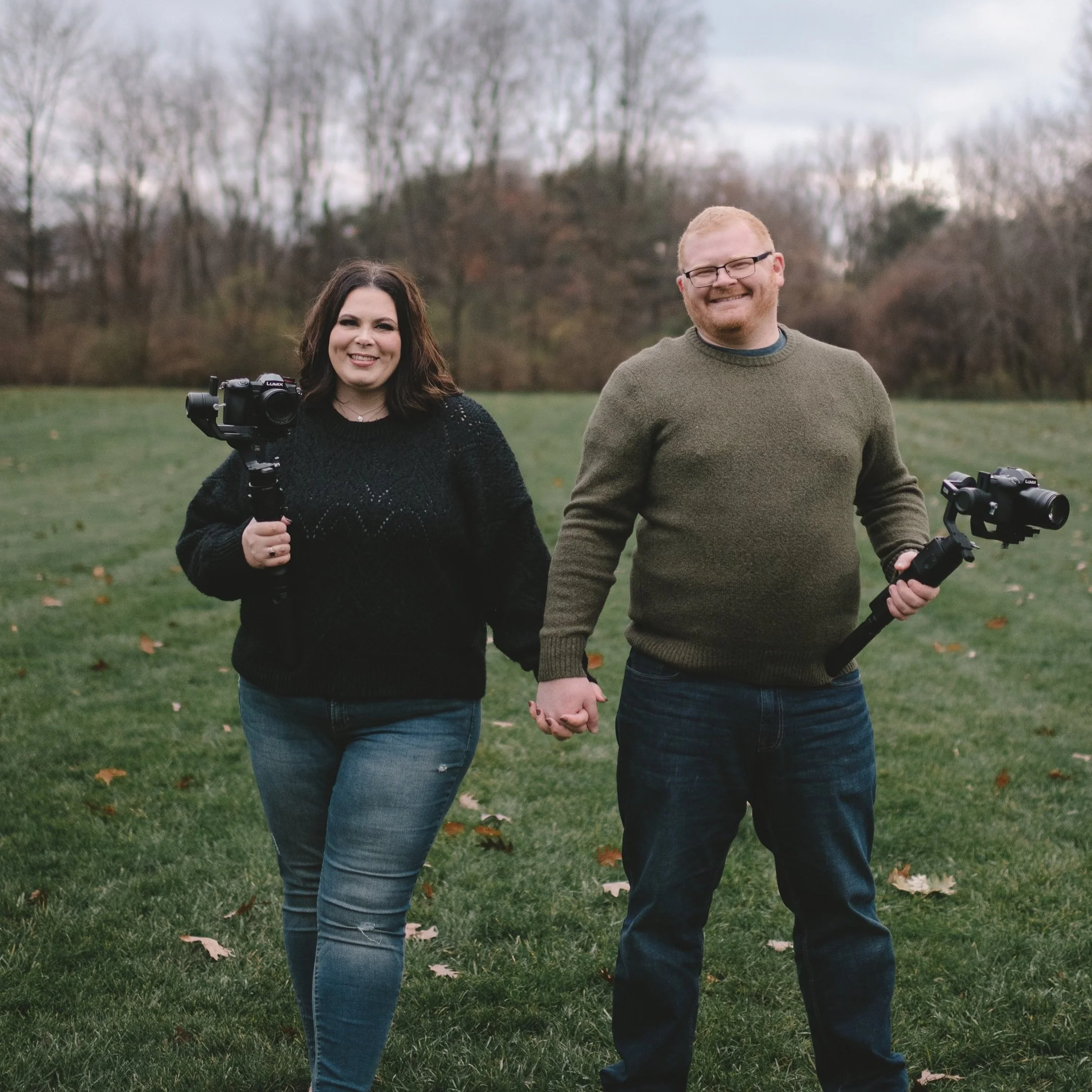 The owners holding hands and smiling in a grassy park, each holding a camera stabilizer with a camera attached.
