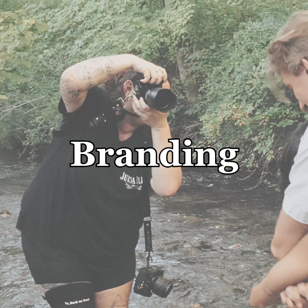 Person with tattoos taking a photograph outdoors by a stream, with the word 'Branding' overlaid.