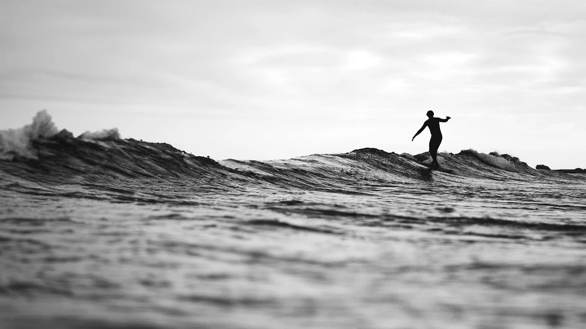 A person surfing on a wave in the ocean, captured in black and white.
