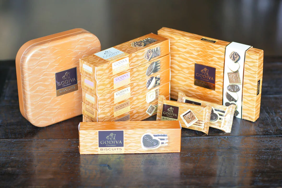An assortment of Godiva chocolates and biscuits in orange packaging on a dark wooden surface.