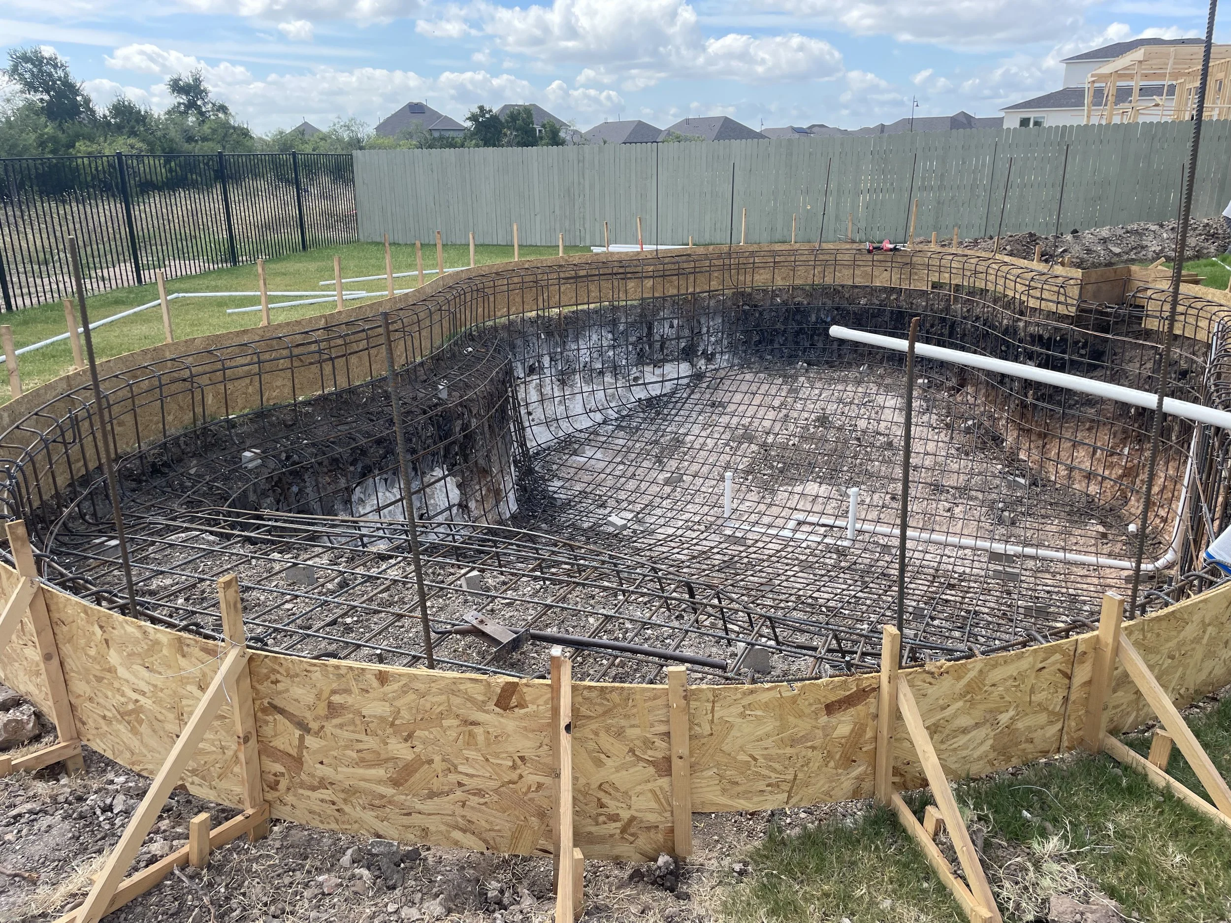 Under construction backyard swimming pool with rebar reinforcement, wooden forms, and PVC pipes.