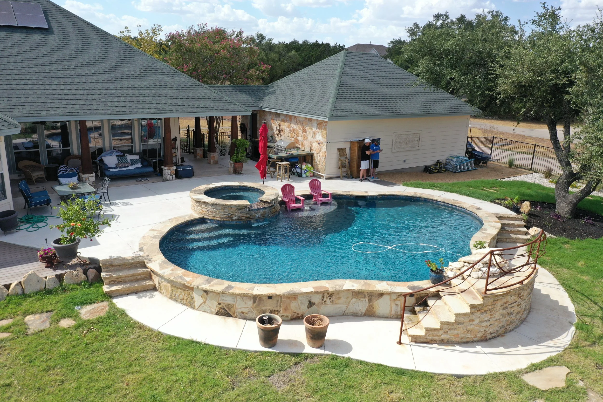 A swimming pool with a stone edge and a small waterfall feature, surrounded by rocks and a black metal fence. A blue sign indicates the pool is a 5-star rated pool.