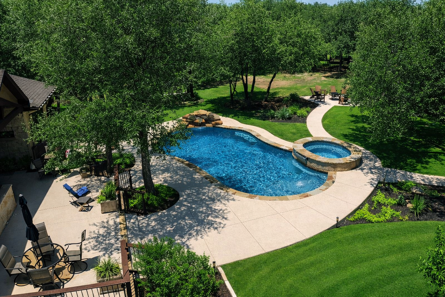 A backyard with a 5-star rated swimming pool and hot tub surrounded by trees and green grass.