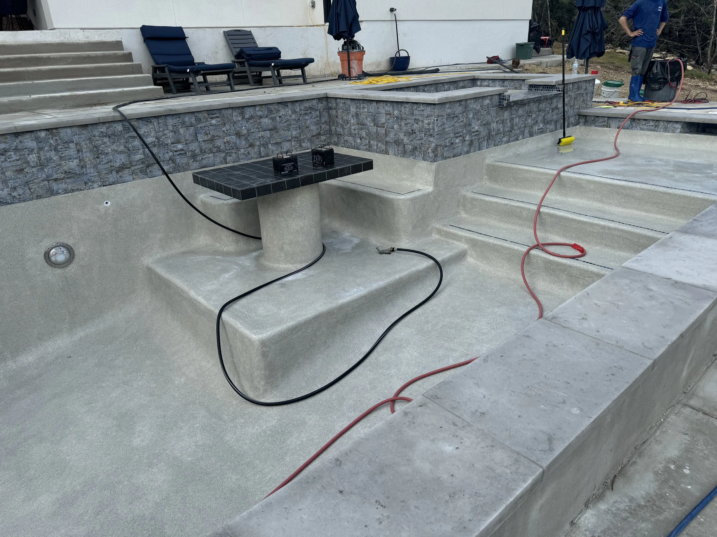 Under construction backyard swimming pool with stairs, a small tiled table, and construction tools.