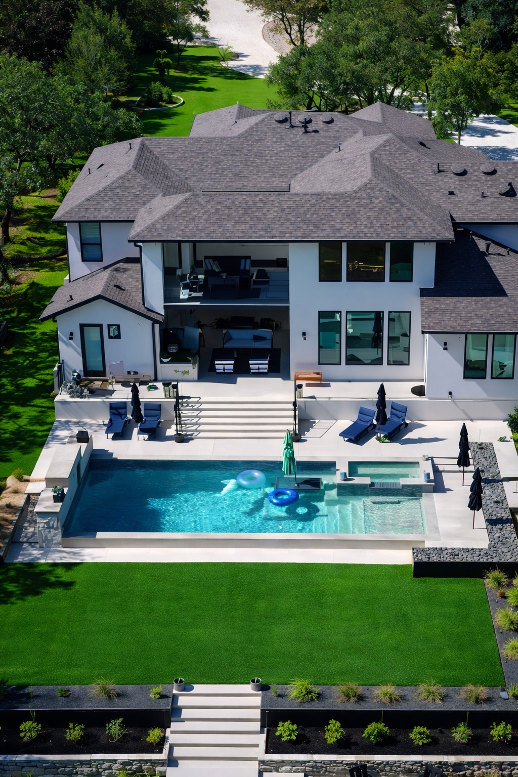 A large modern two-story house with a swimming pool in the backyard, surrounded by green lawn and trees.