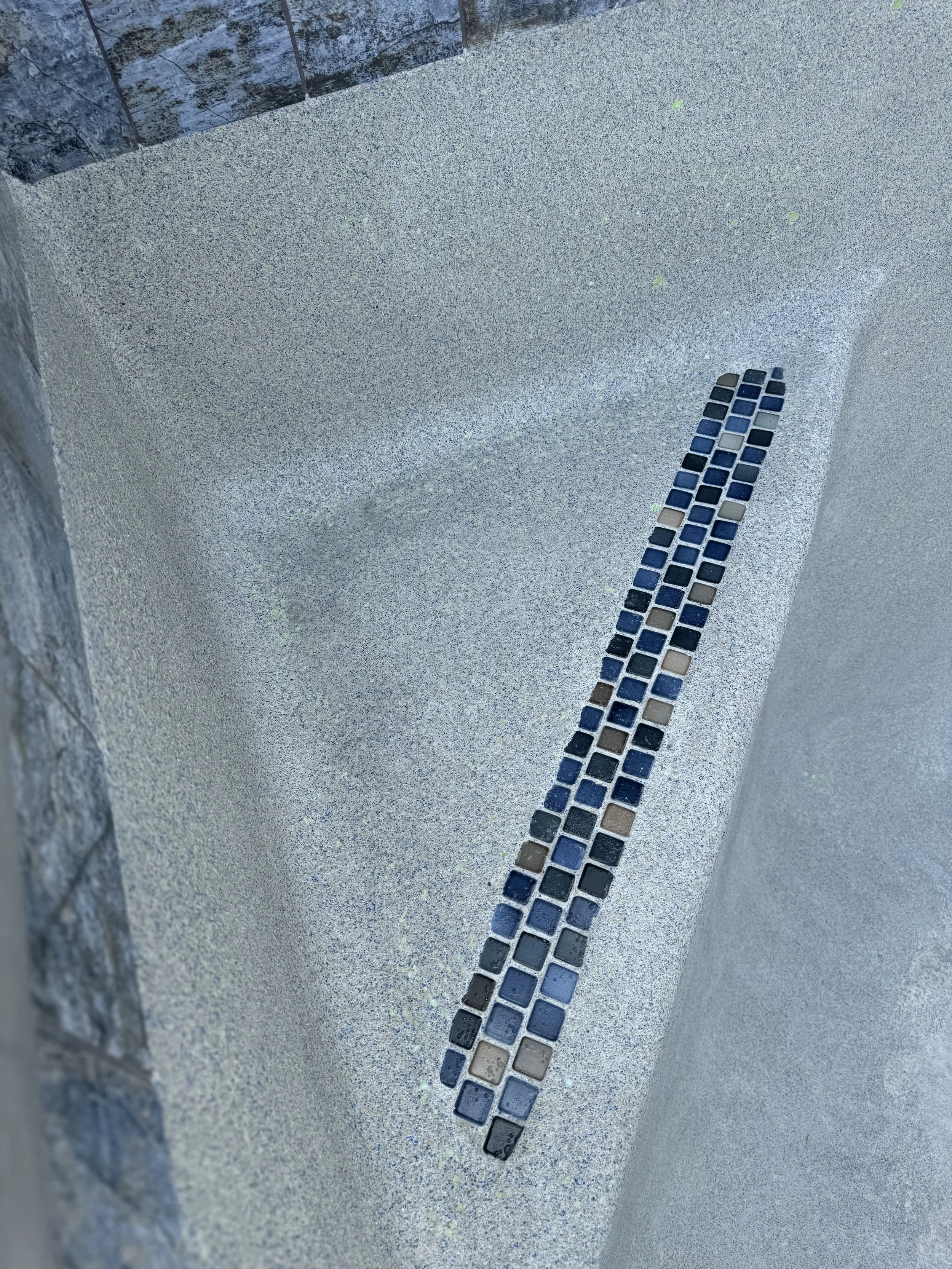 Close-up of a shower area with textured white walls, a mosaic tile drain cover, and a stone wall on the left side.