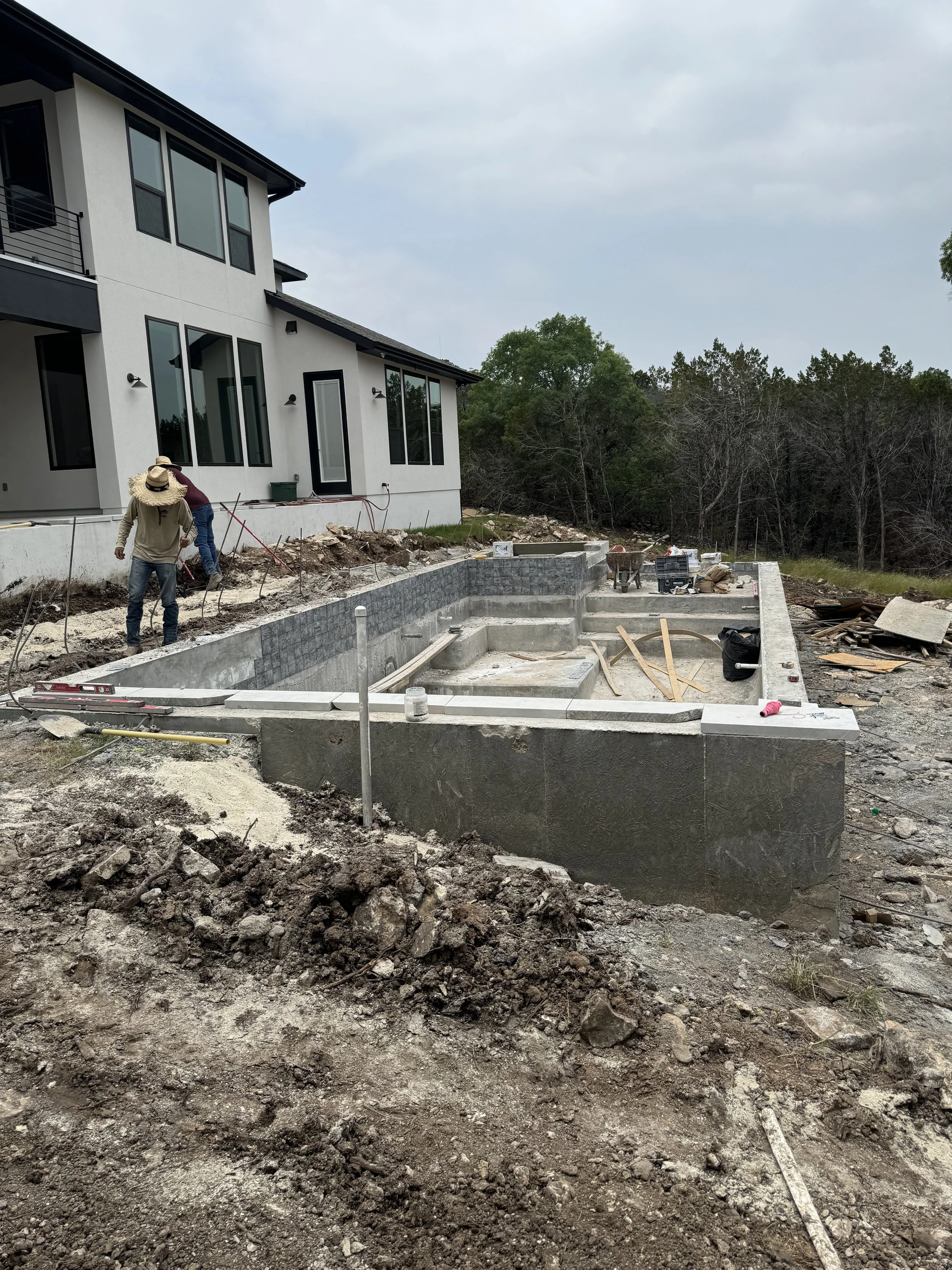 Construction workers building a pool in the backyard of a house under construction.