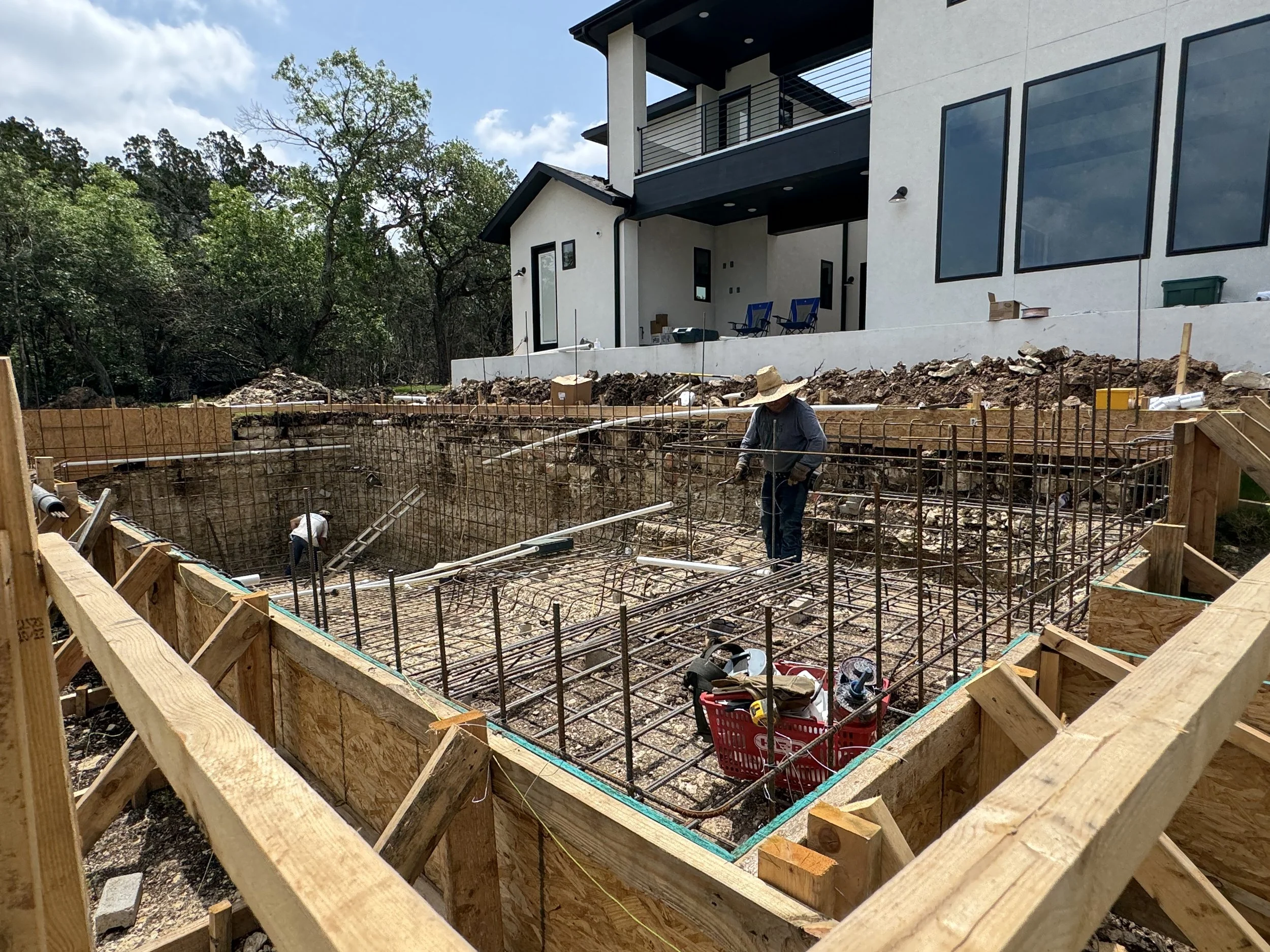 Construction workers building a foundation with rebar framework for a new structure in front of a modern white house.