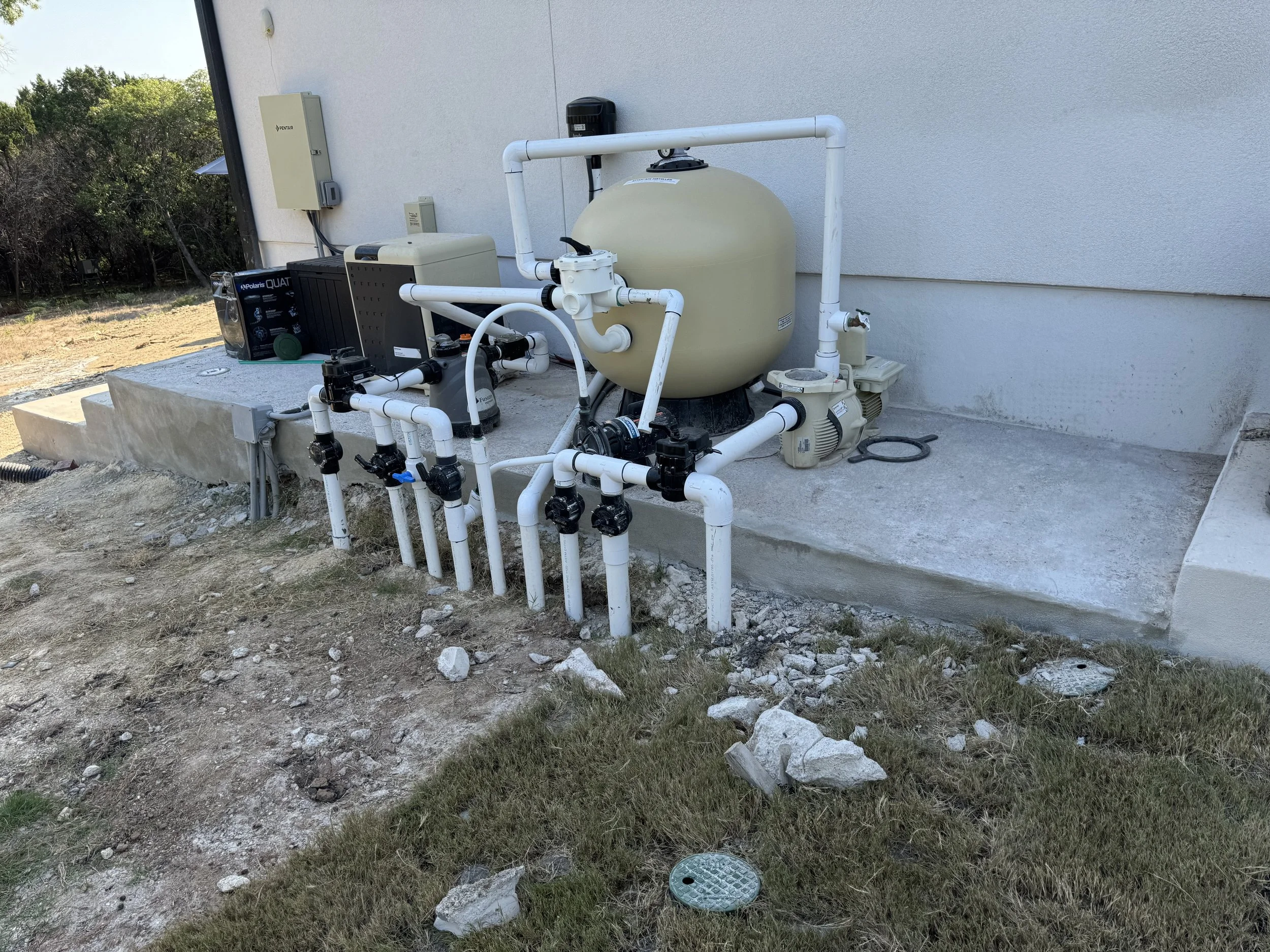 Pool equipment including a filter, pump, and pipes installed outside a house on a concrete slab.