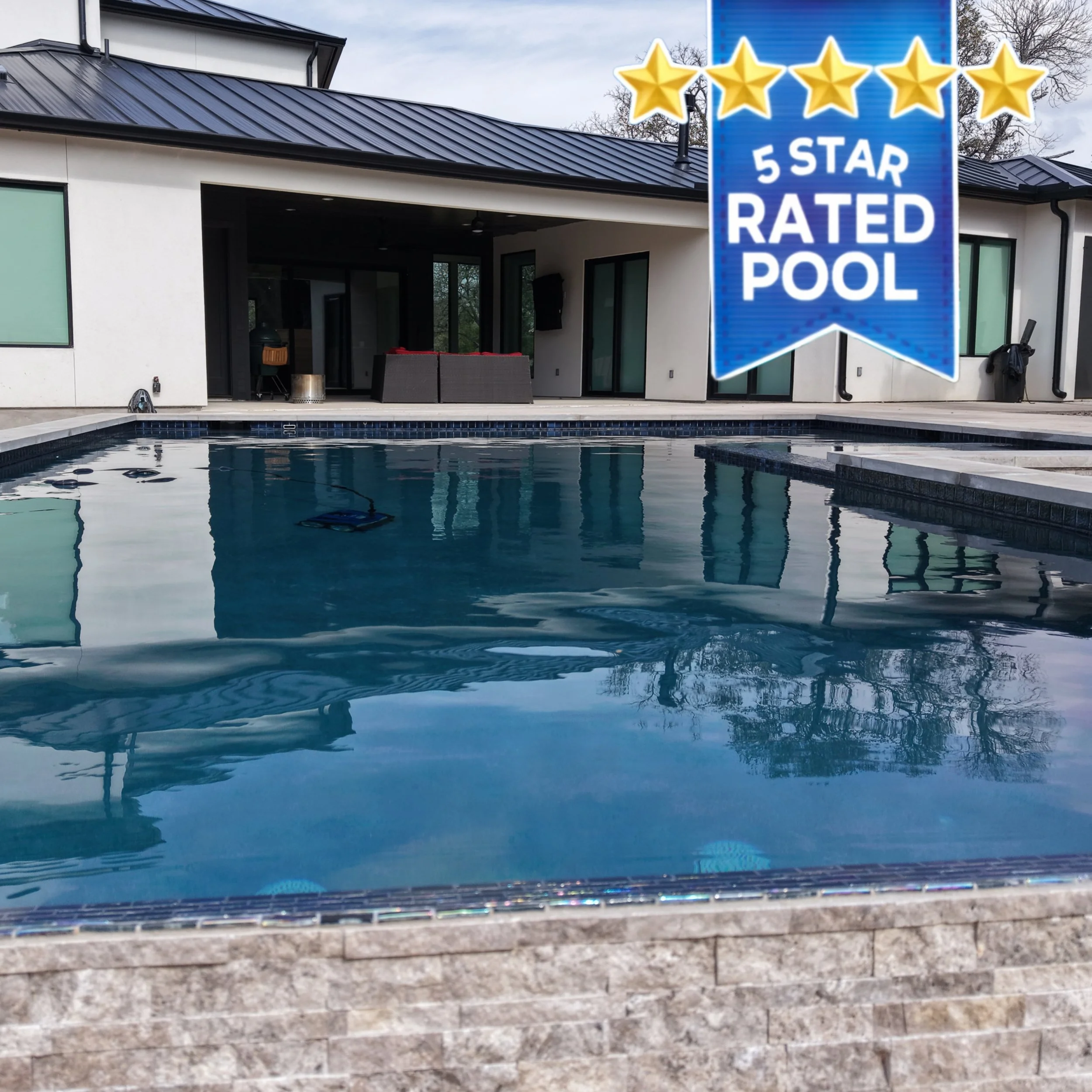 Aerial view of a modern house with a black metal roof, a small backyard with a rectangular swimming pool, concrete patio, fenced yard, parked car, and some greenery.