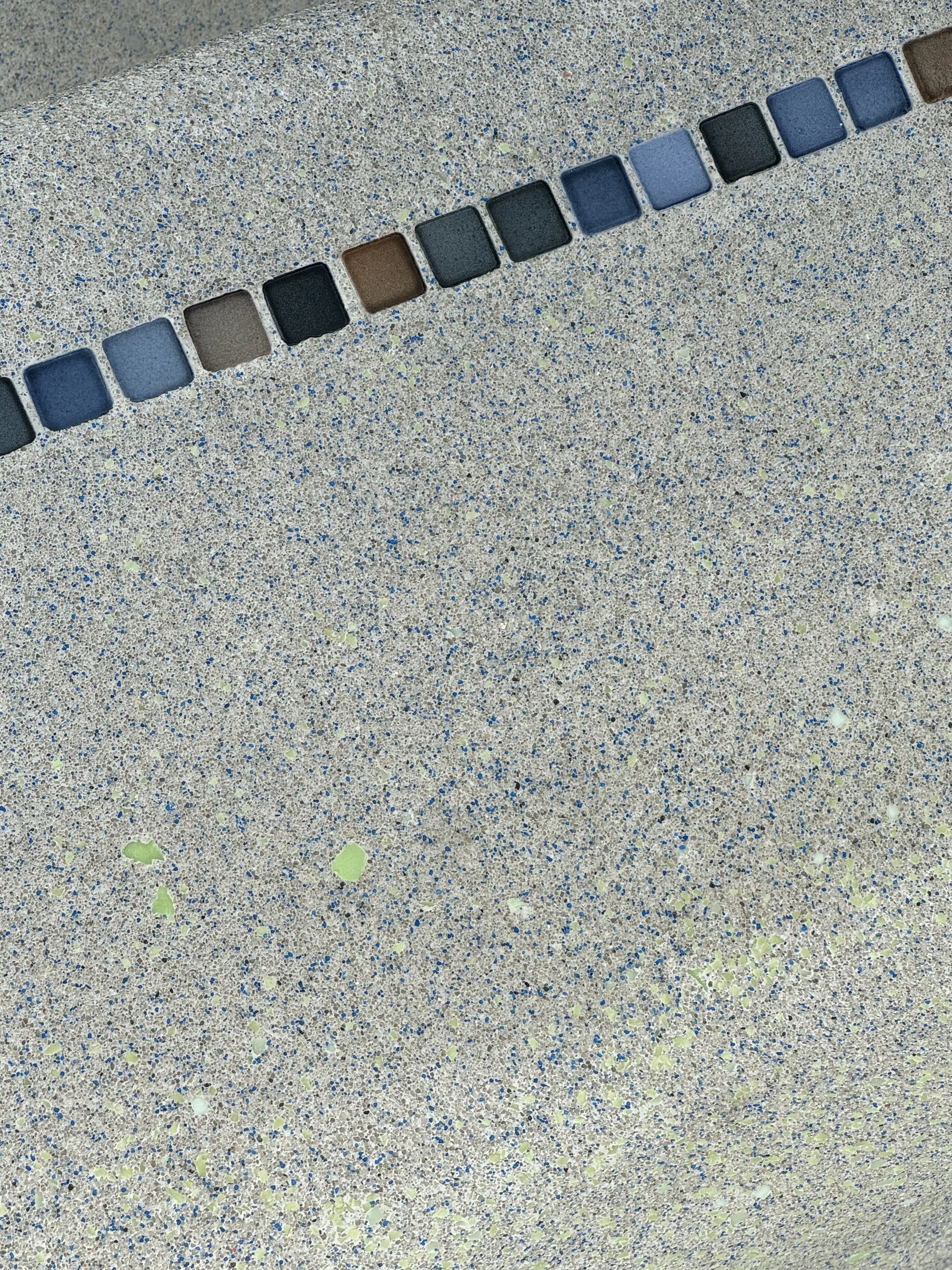 Colorful square tiles arranged along the edge of a speckled beige countertop.