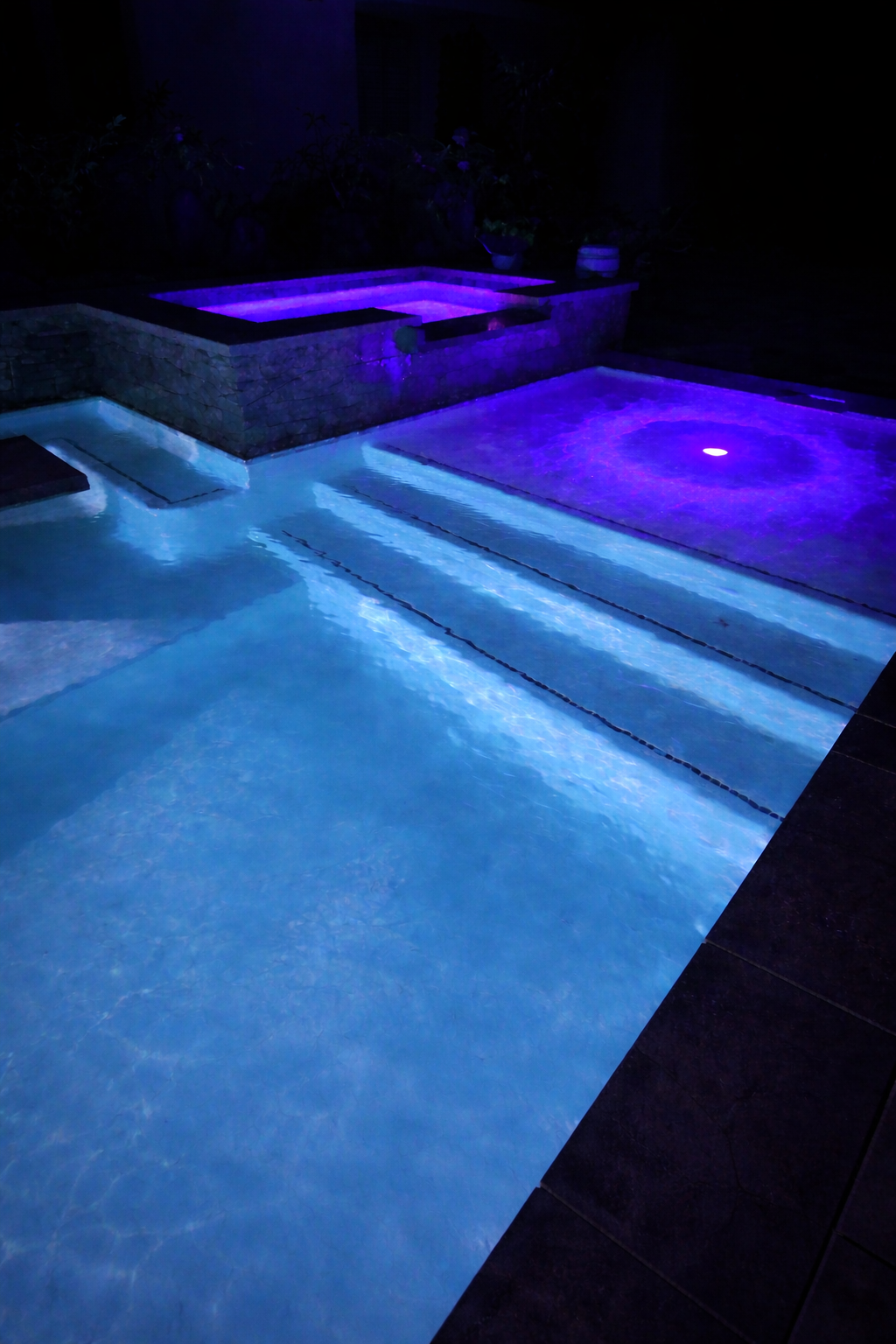 Nighttime view of a swimming pool illuminated with blue and purple lights.