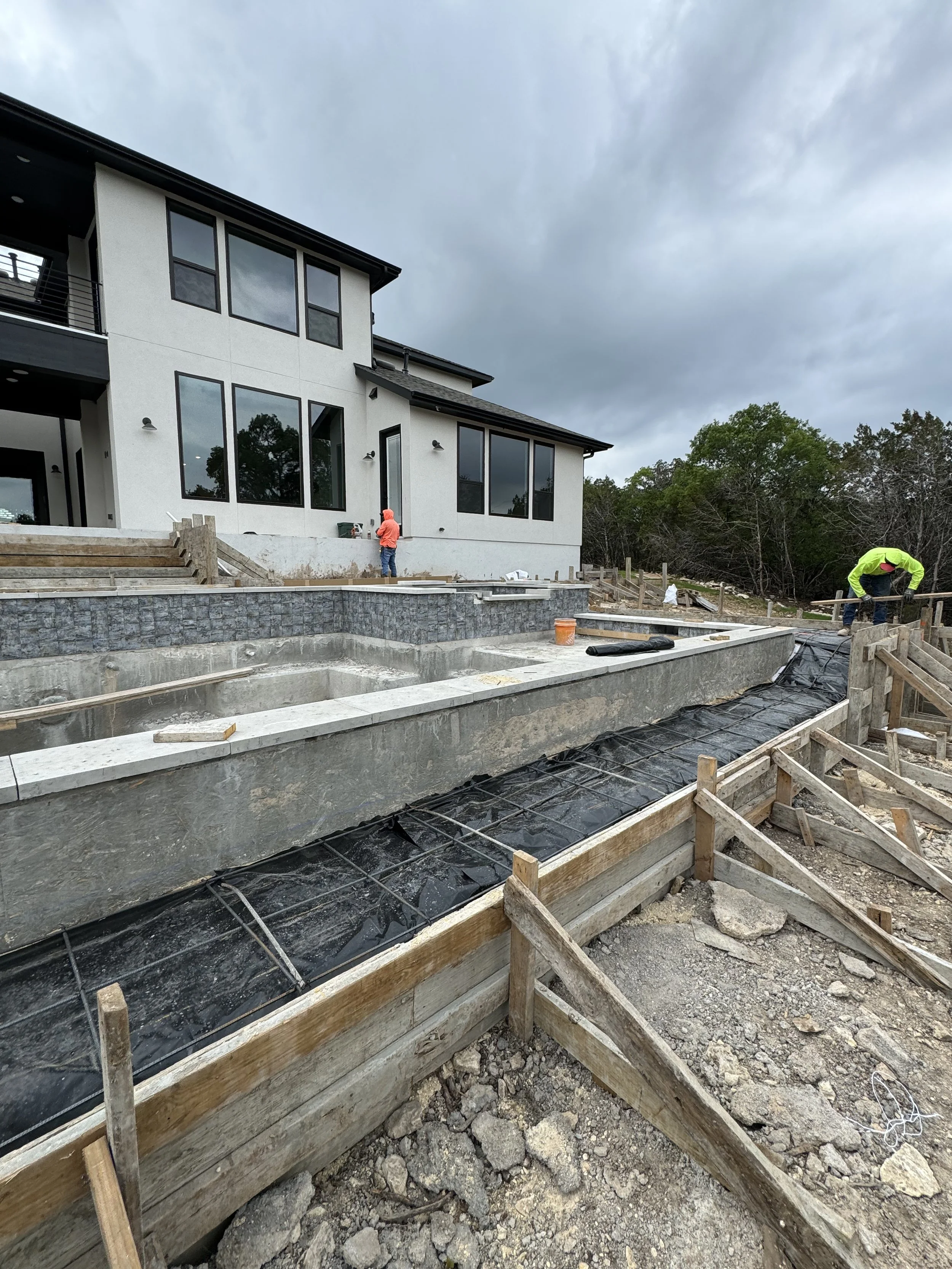 Construction site with workers building a swimming pool in front of a modern house. Overcast sky.
