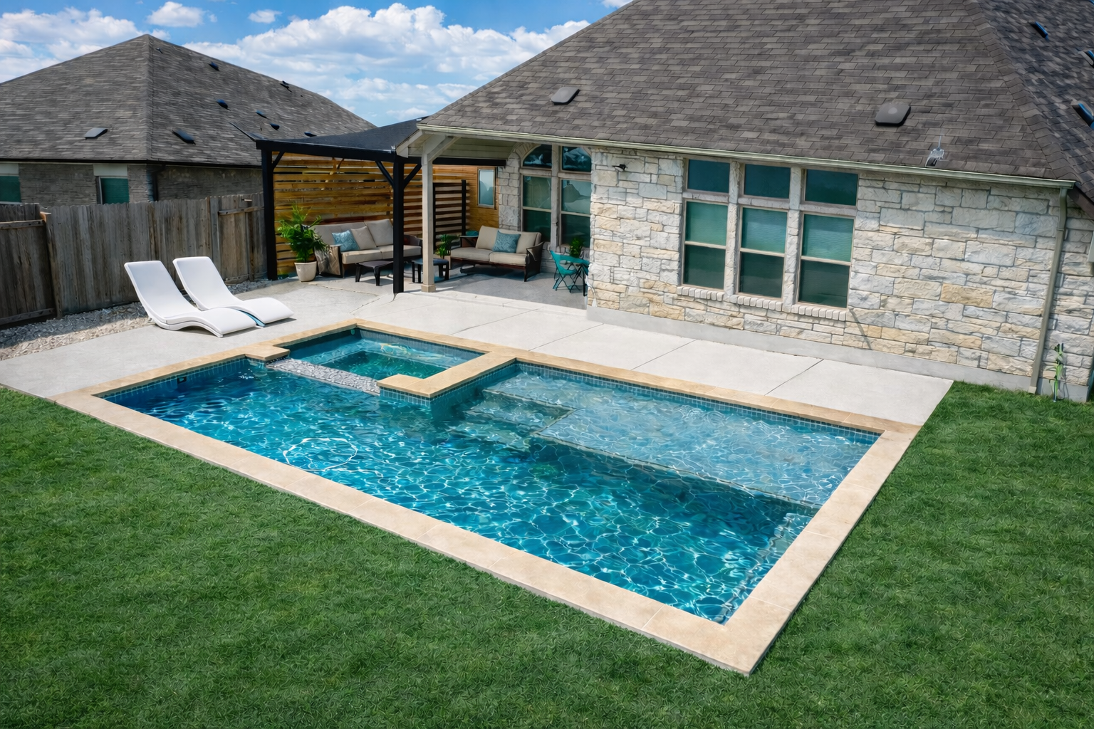 Backyard with in-ground swimming pool, two white lounge chairs, patio furniture including two couches and a small table under a black pergola, green grass, wooden fence, adjacent house with stone exterior, cloudy blue sky