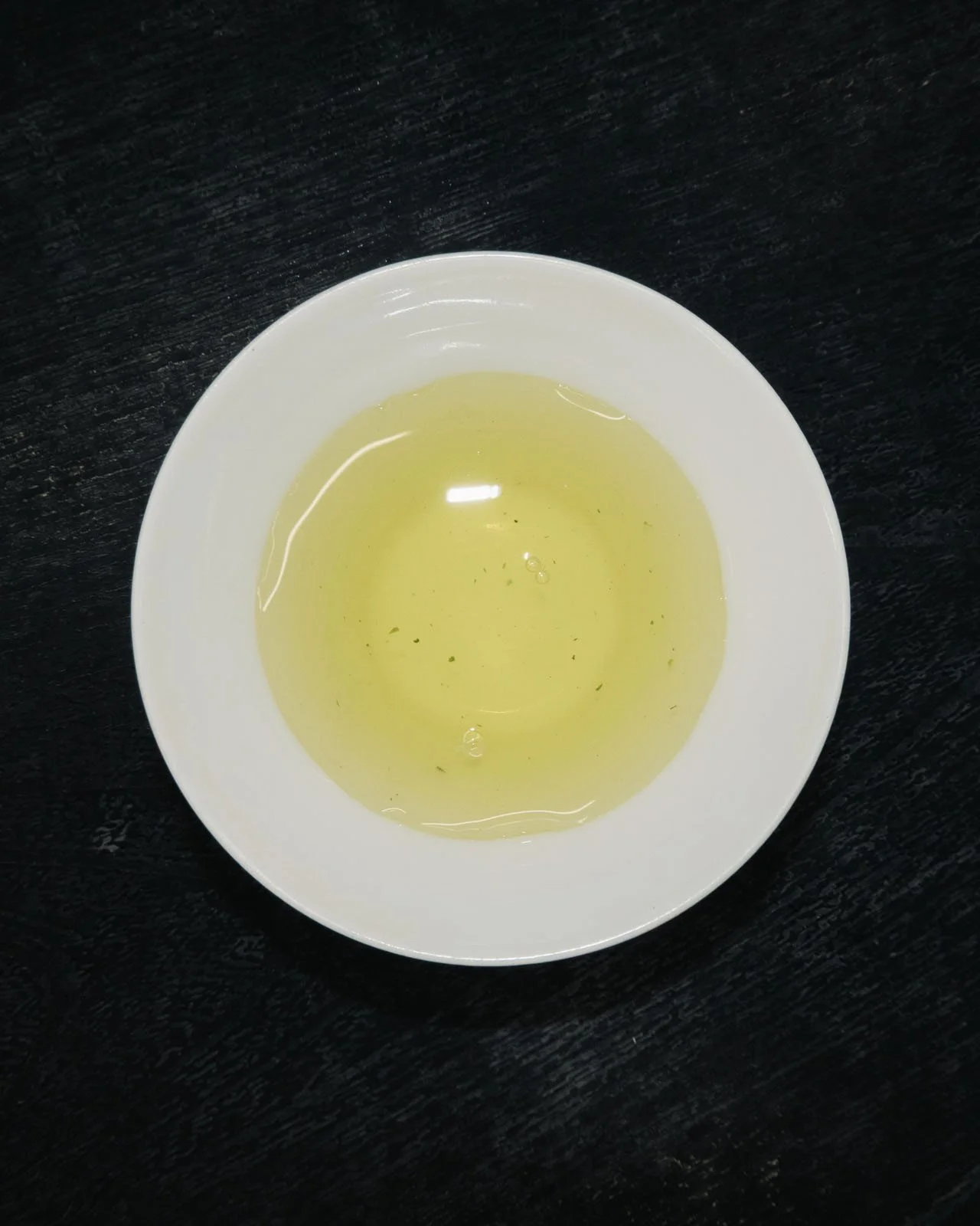 Pale green brewed tea in a white tasting cup, showing the liquor color that tea competition judges score