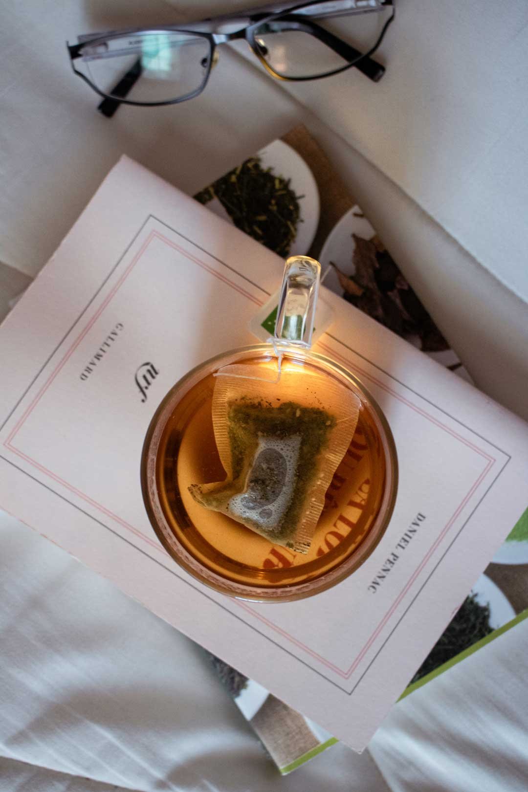 A hot cup of herbal tea with books and glasses on a bed