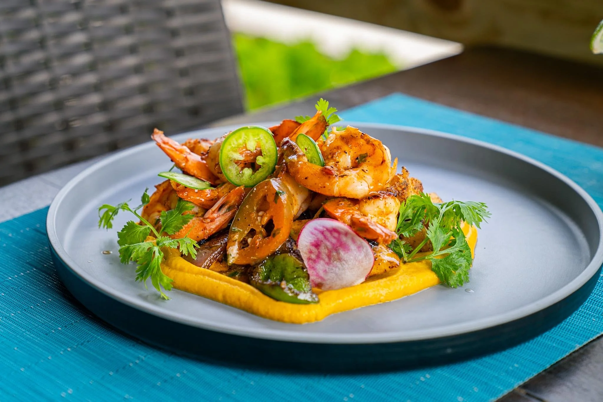 A plate of seafood including shrimp, garnished with jalapeños, radish slices, cilantro, and avocado slices, served on a yellow sauce base.