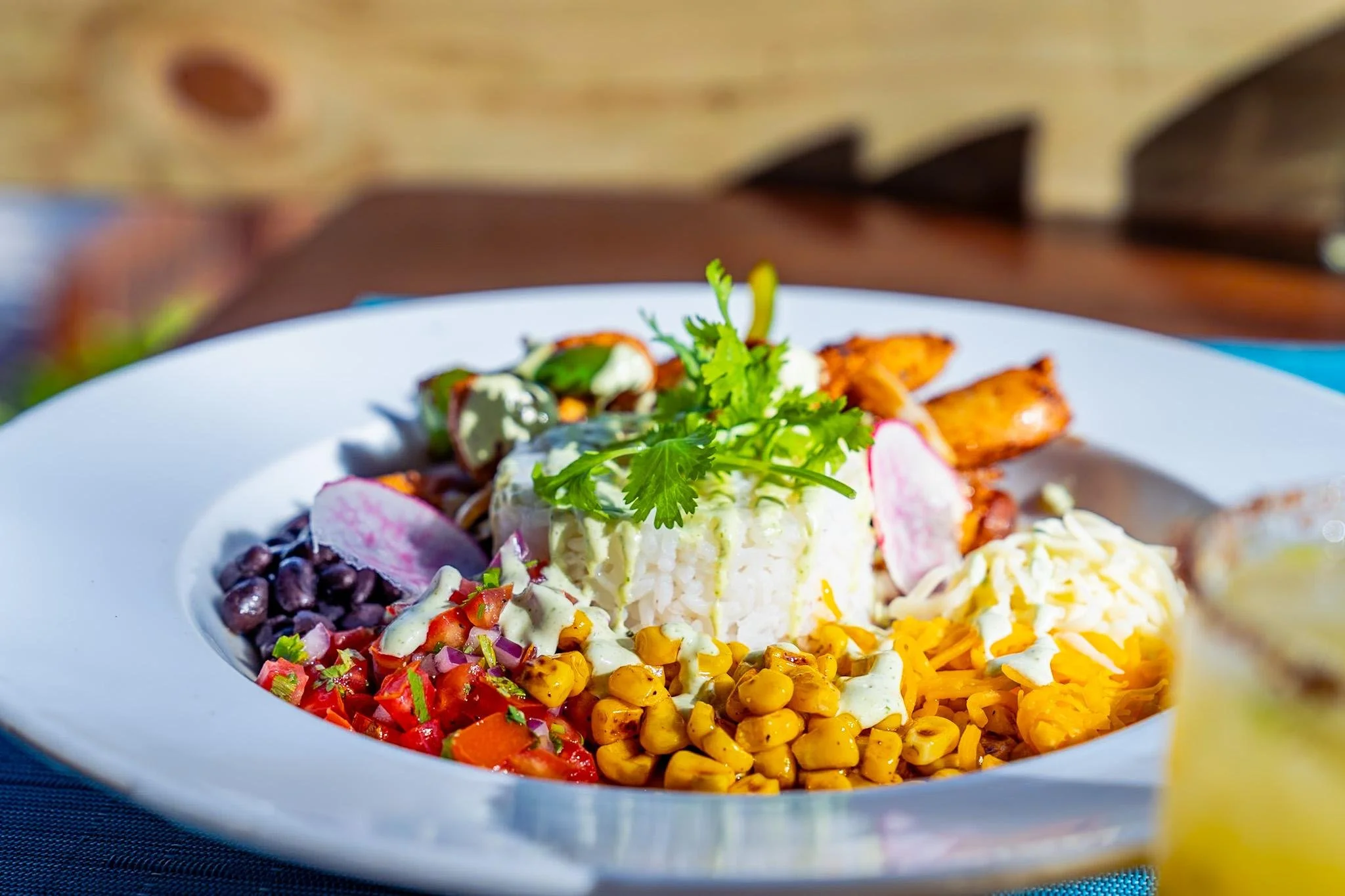 Colorful Mexican-style salad with corn, beans, tomatoes, radishes, shredded cheese, grilled chicken, and fresh cilantro on a white plate.