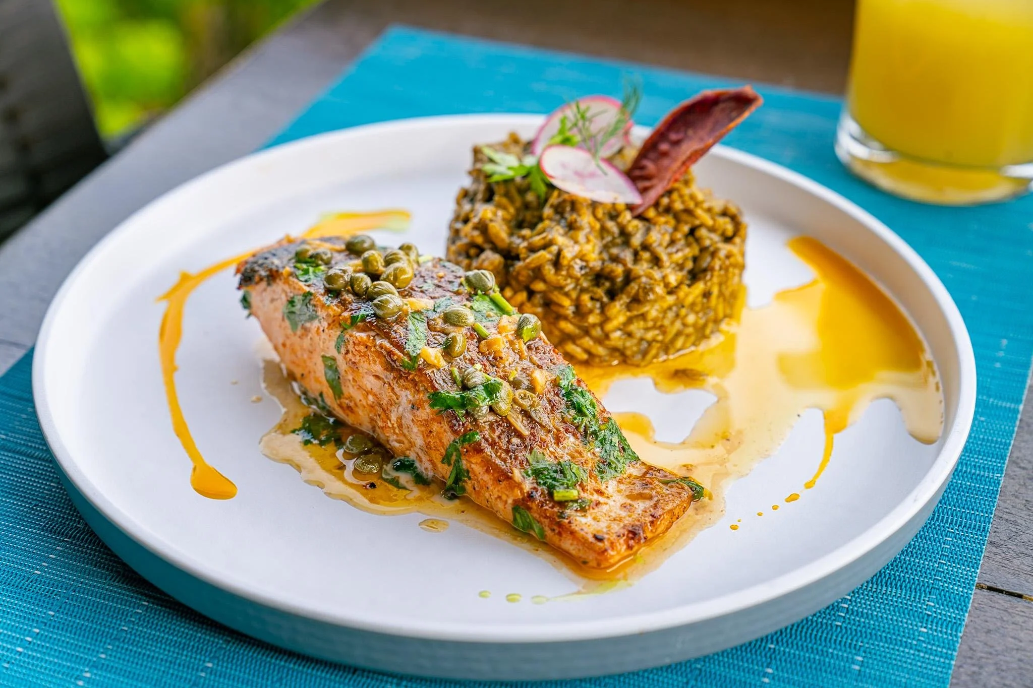 Grilled salmon with green peppercorn sauce, served with a side of seasoned rice garnished with a radish and parsley, on a white plate with sauce drizzled around.