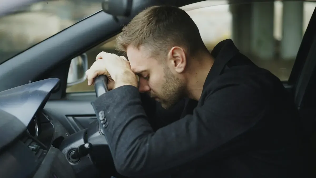 Man sitting in a car with his head resting on the steering wheel