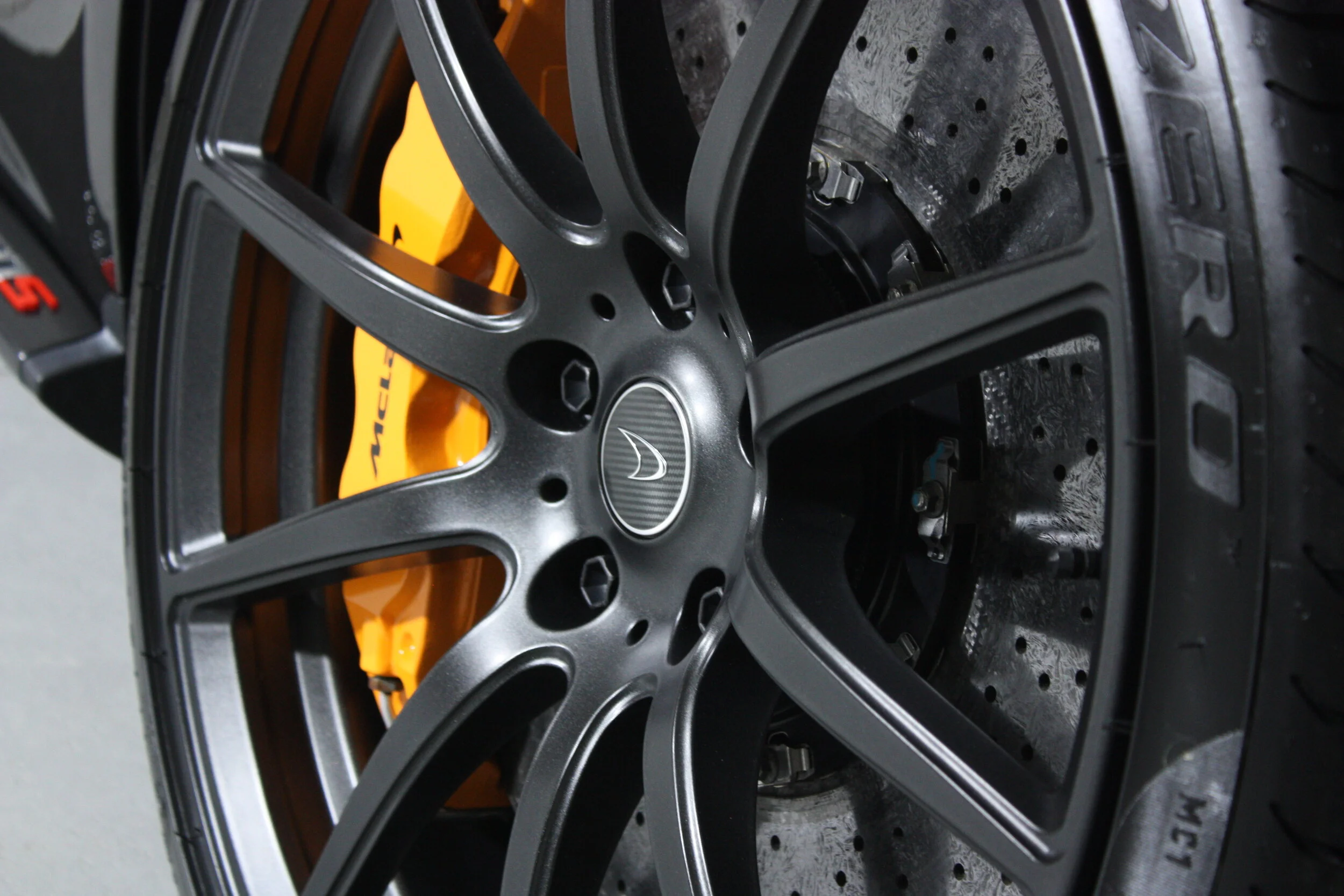 Close-up of a black Porsche wheel with a yellow brake caliper visible behind, and a perforated brake disc.