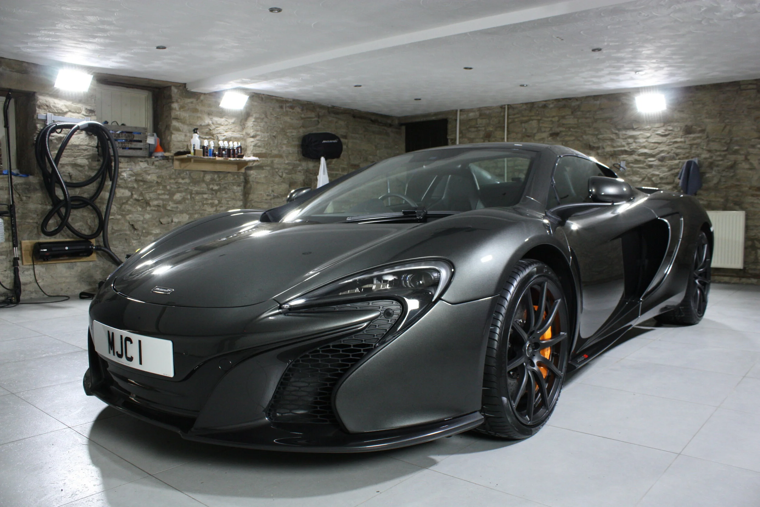 A black sports car, possibly a McLaren, parked in a garage with stone walls and a tiled floor.