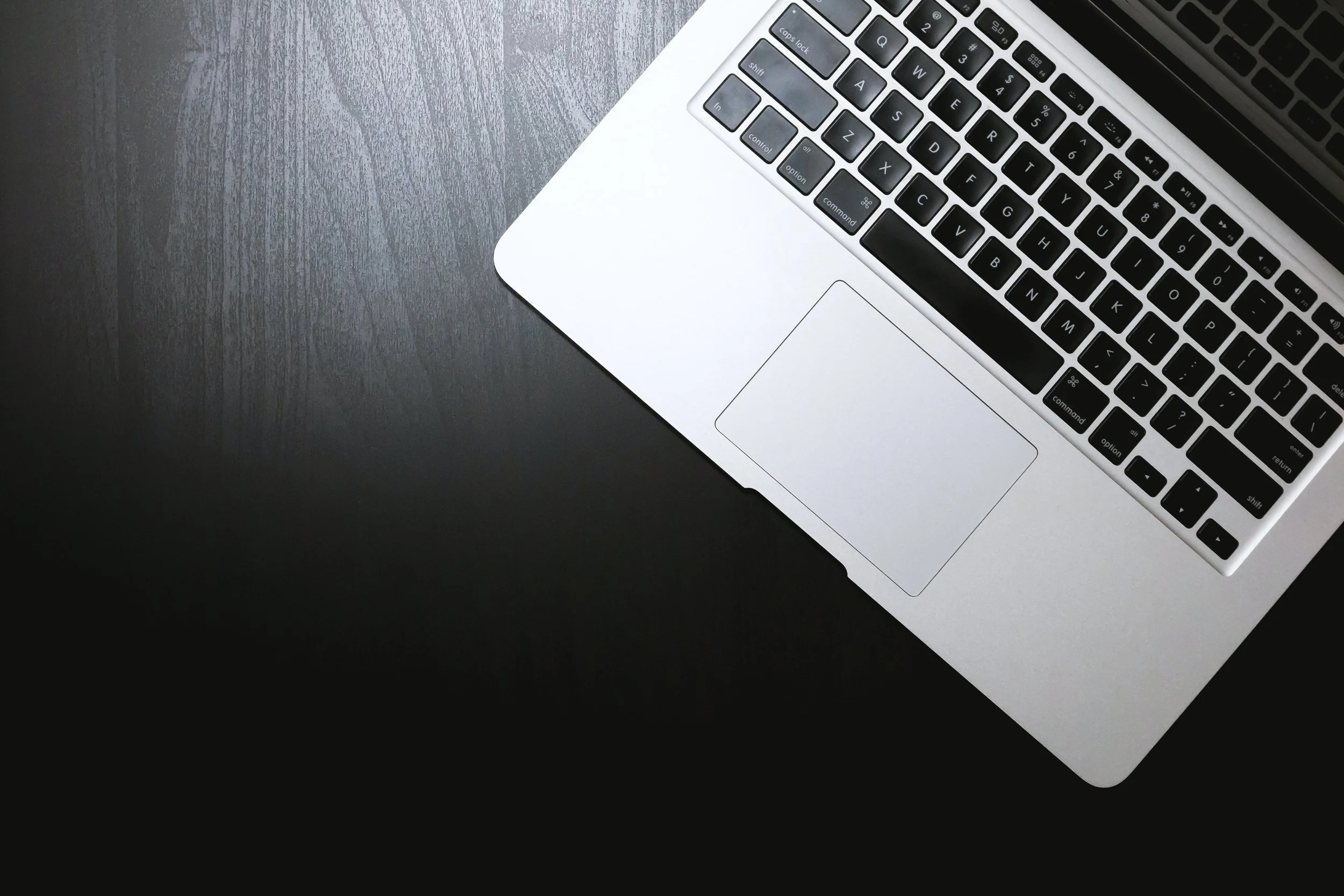 Close-up of an open silver laptop on a dark wooden desk, showing the keyboard and trackpad.