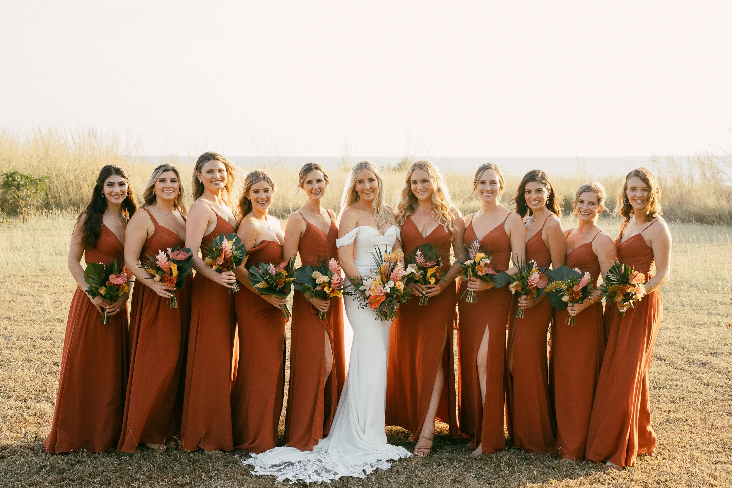 Bridesmaids holding tropical bouquets in blush, orange and terracotta tones at Hacienda Pinilla, Costa Rica.