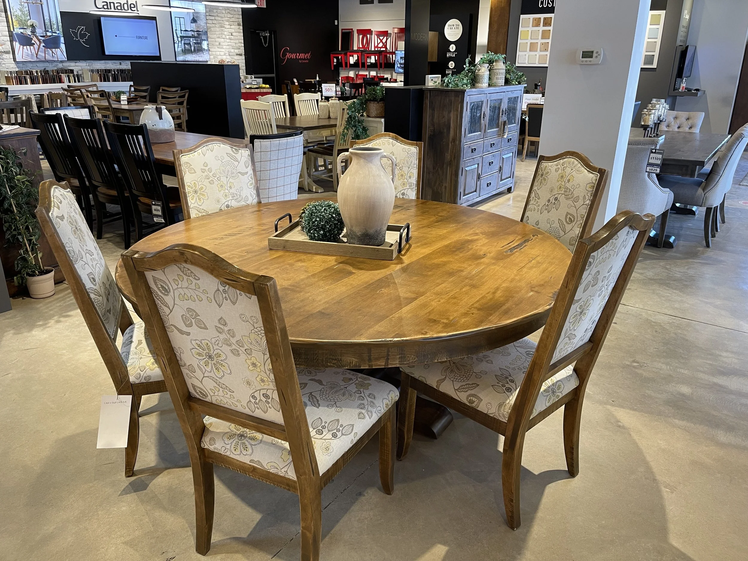 Round wooden dining table with six upholstered chairs in a furniture store display.
