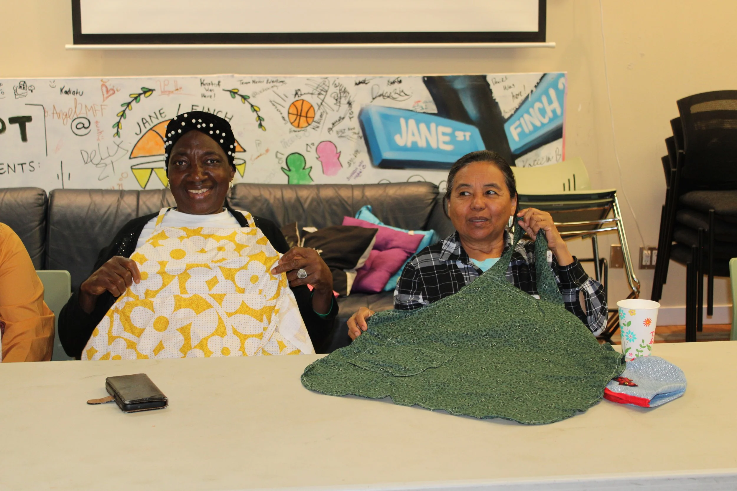 Two participants in a sewing program at the Jane/Finch Centre showing their handmade creations