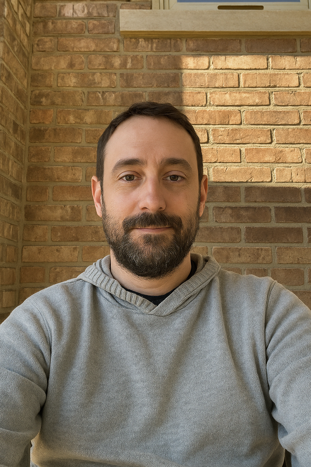CEO with a beard and short dark hair taking a selfie indoors with a brick wall background.