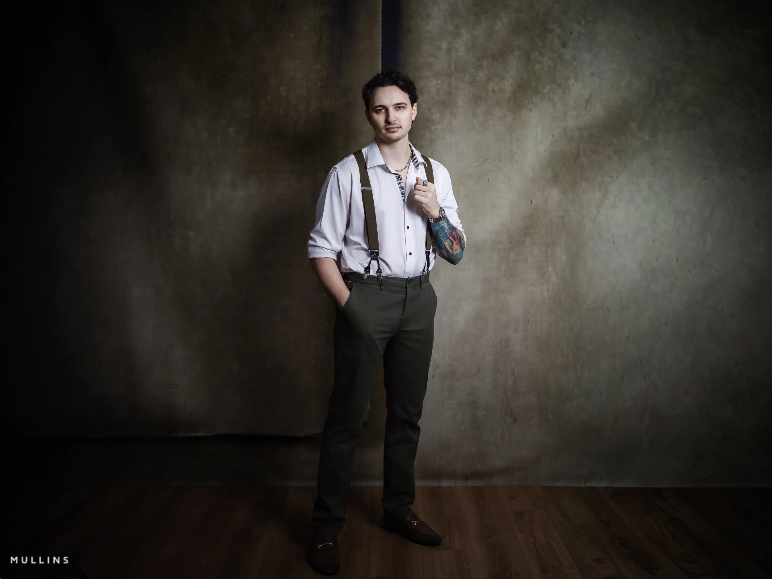 Full-length business branding portrait of young entrepreneur standing in studio wearing white shirt, braces and tailored trousers.