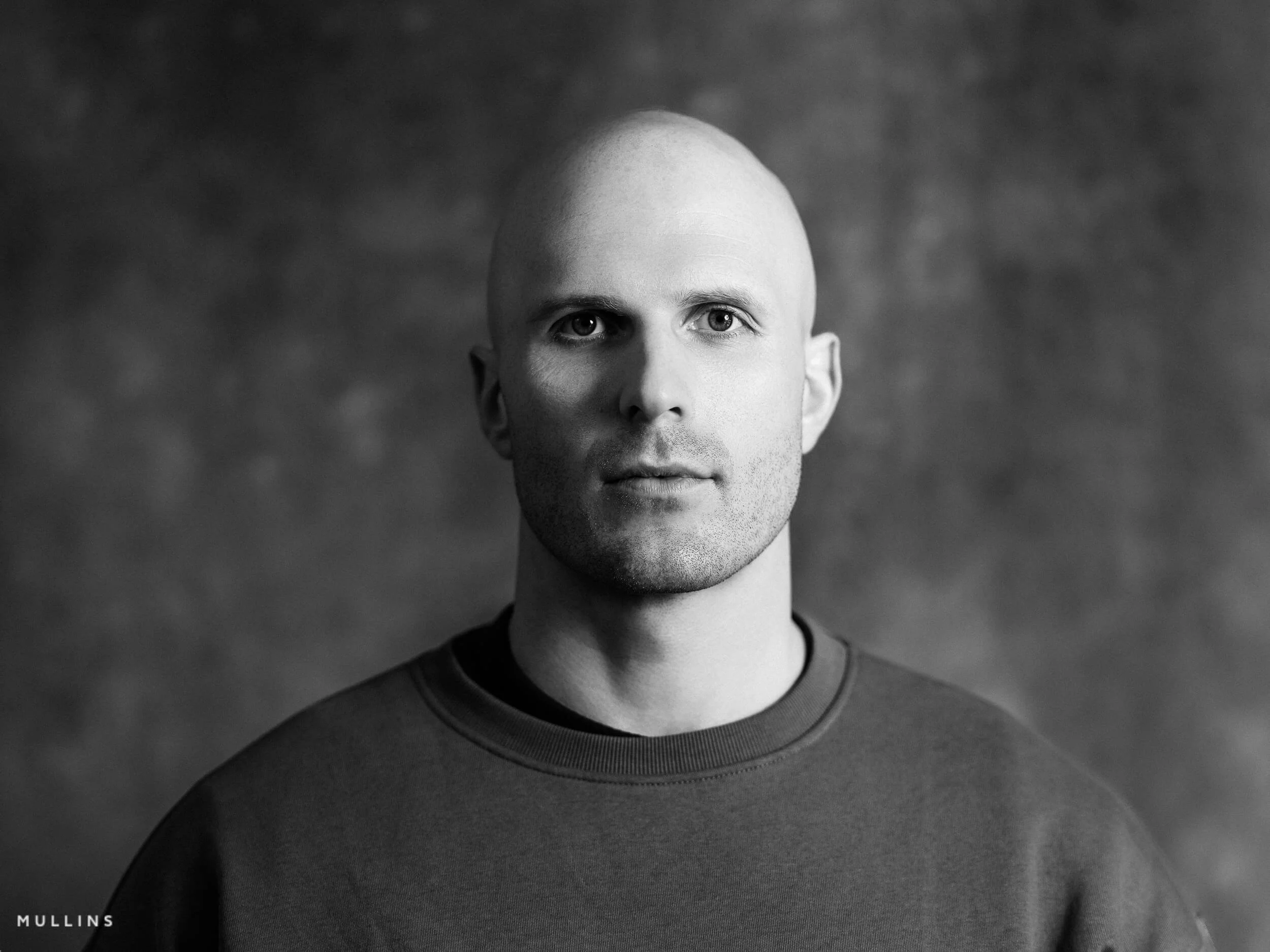 Monochrome front-facing actor headshot of Ian McIntyre in studio wearing a grey sweatshirt.