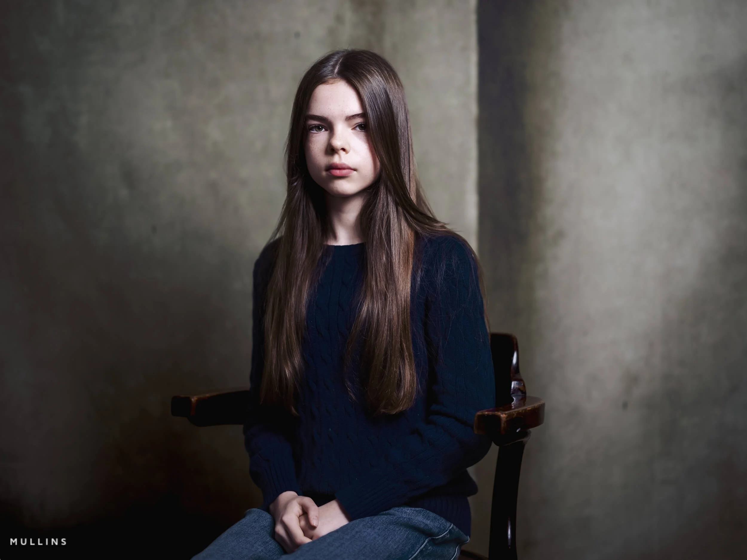 Head and shoulders portrait of a young female actor seated in a chair in the studio, wearing a dark knit jumper.