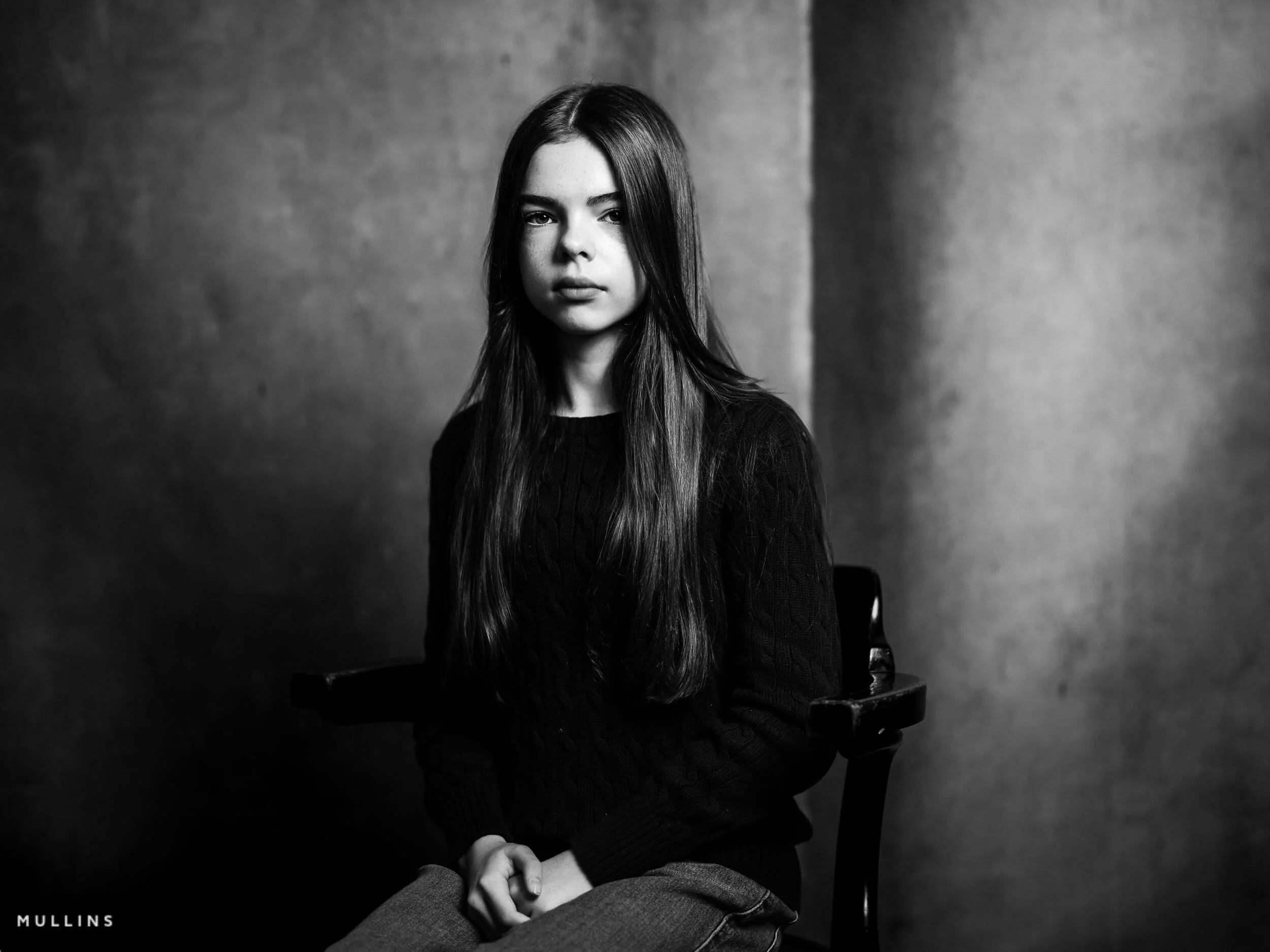 Black and white head and shoulders portrait of a young female actor seated in a chair, wearing a dark knit jumper.