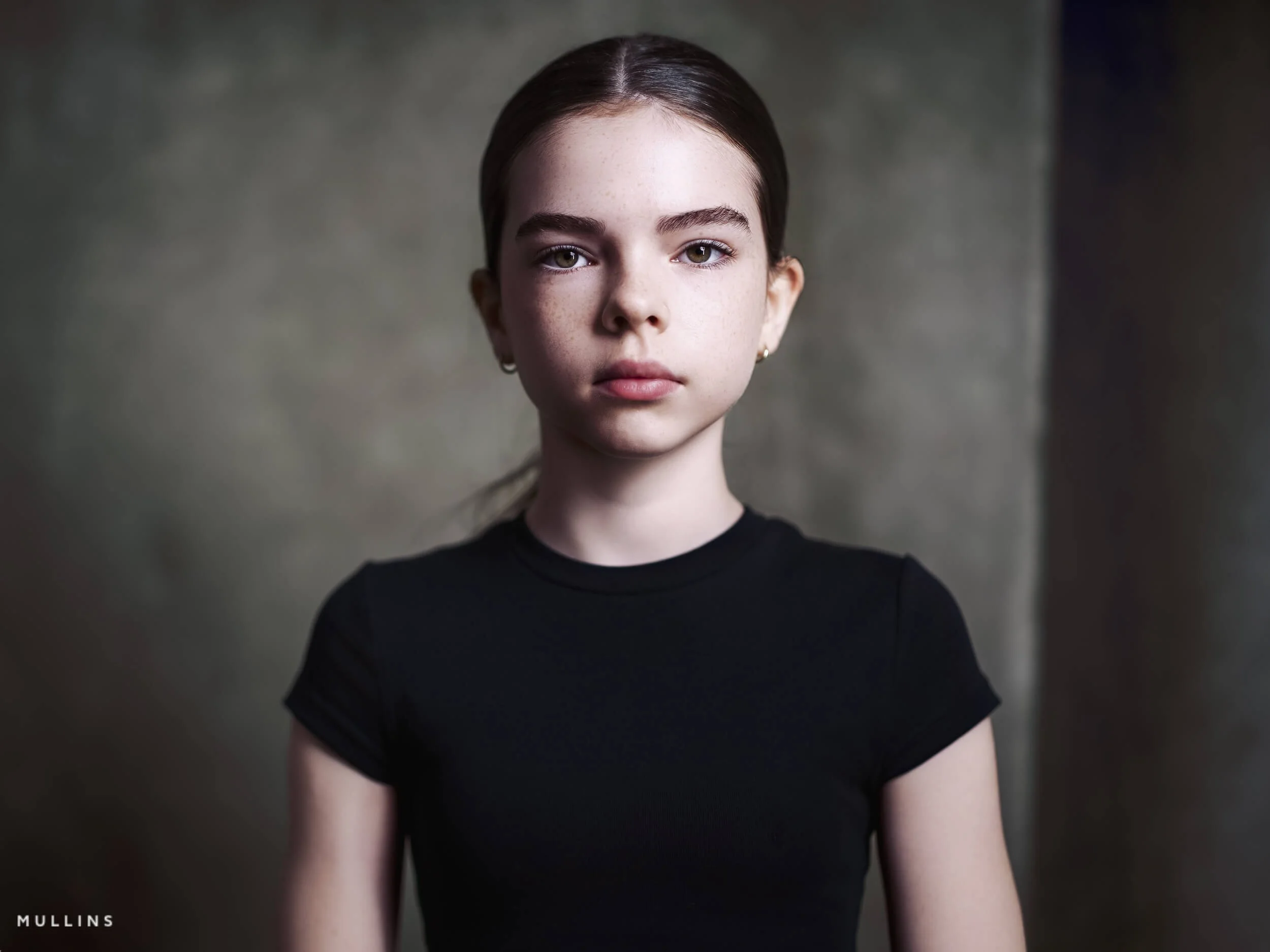 Close portrait of a young female actor wearing a black top against a textured studio backdrop.