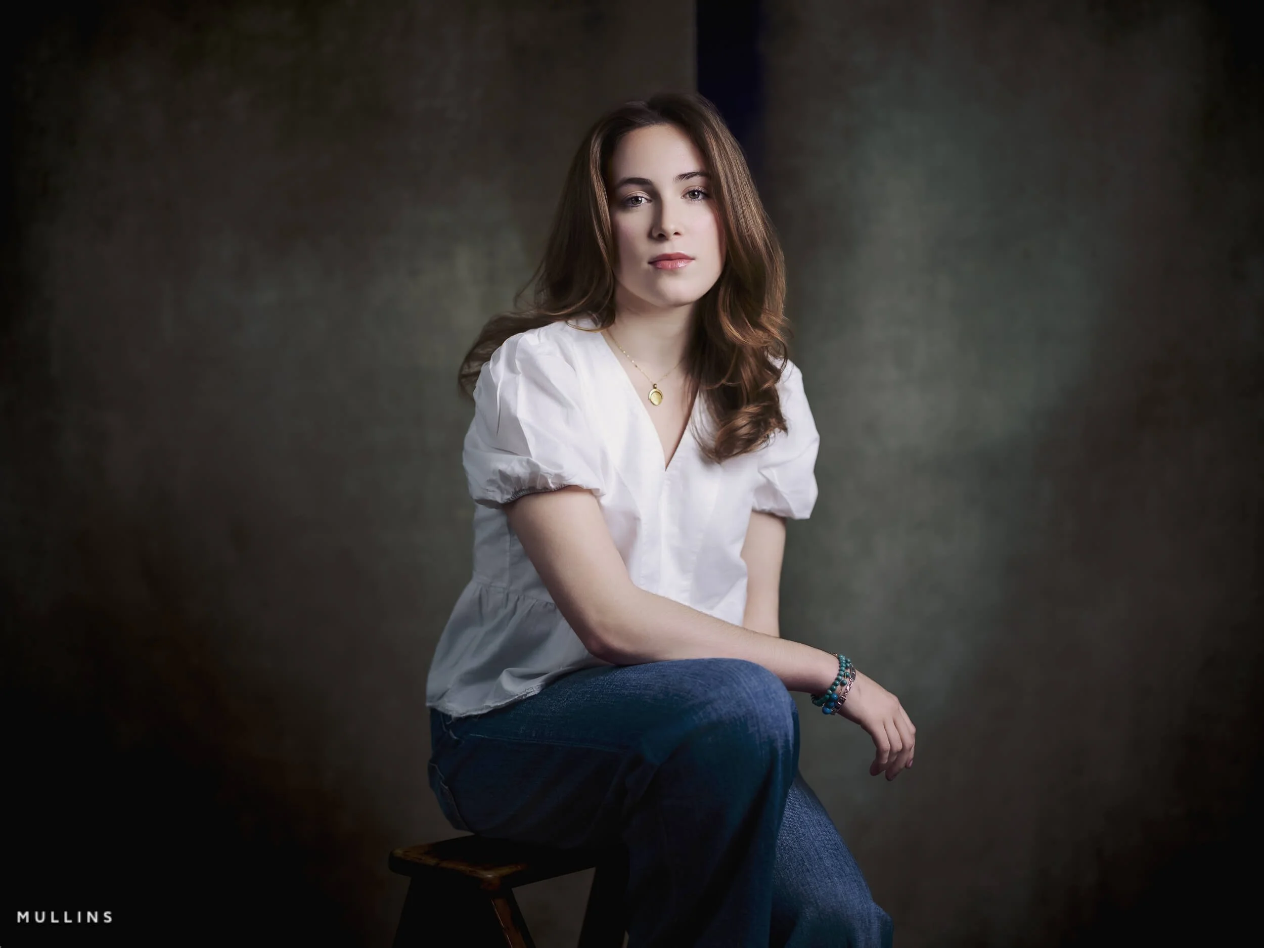 Full-length actor portfolio photo of a young actress standing in jeans and a black top against a dark studio backdrop.