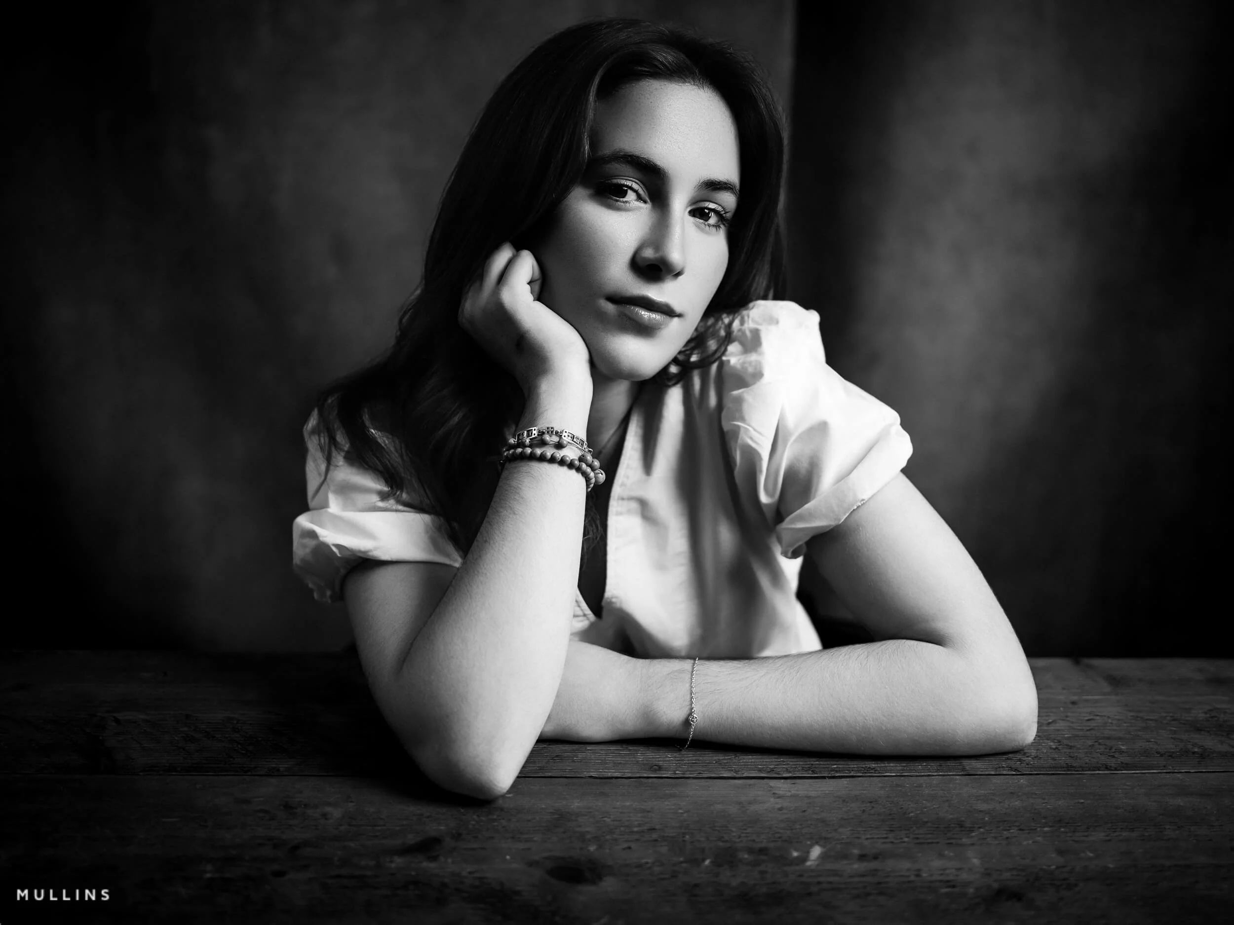 Monochrome actor headshot of a young lady sat at a desk.