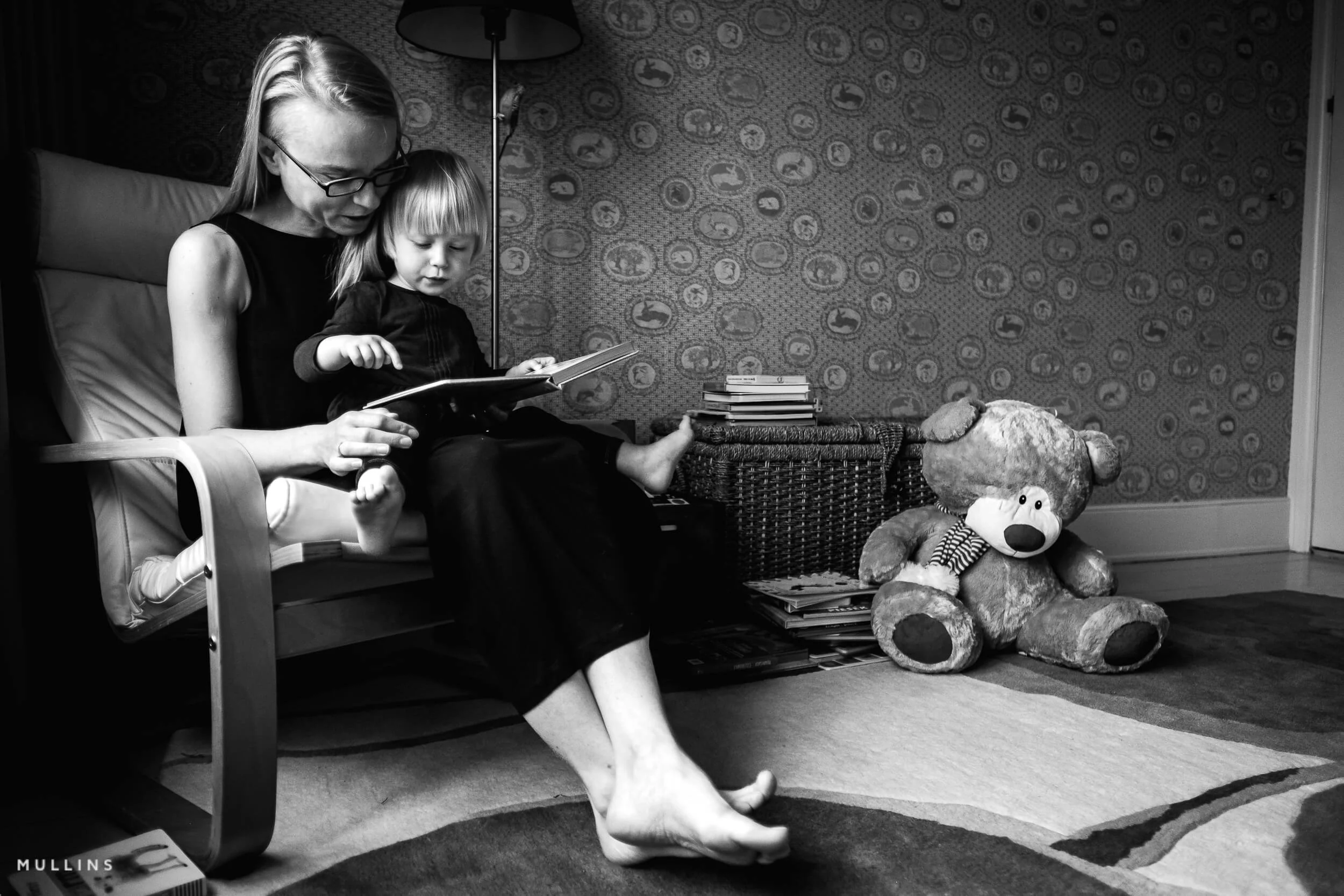 A mother and young daughter sitting on a chair reading a book