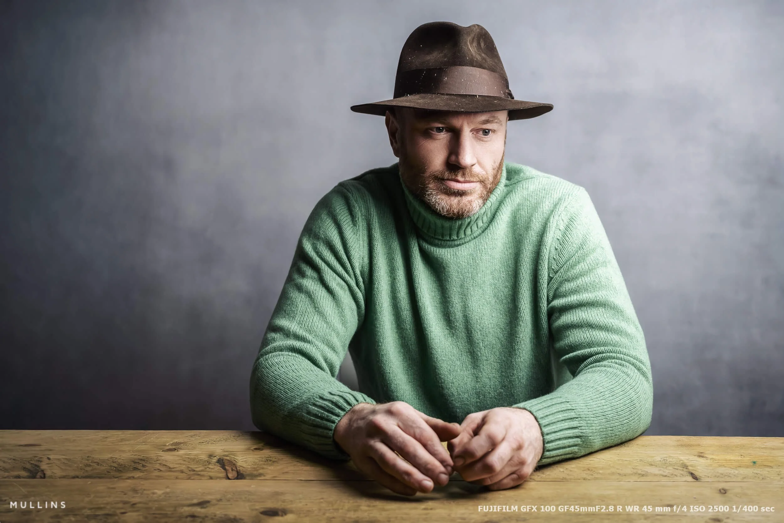 A portrait of a farmer sat behind a desk in a photographic studio.  Taken with Fujifilm GFX.