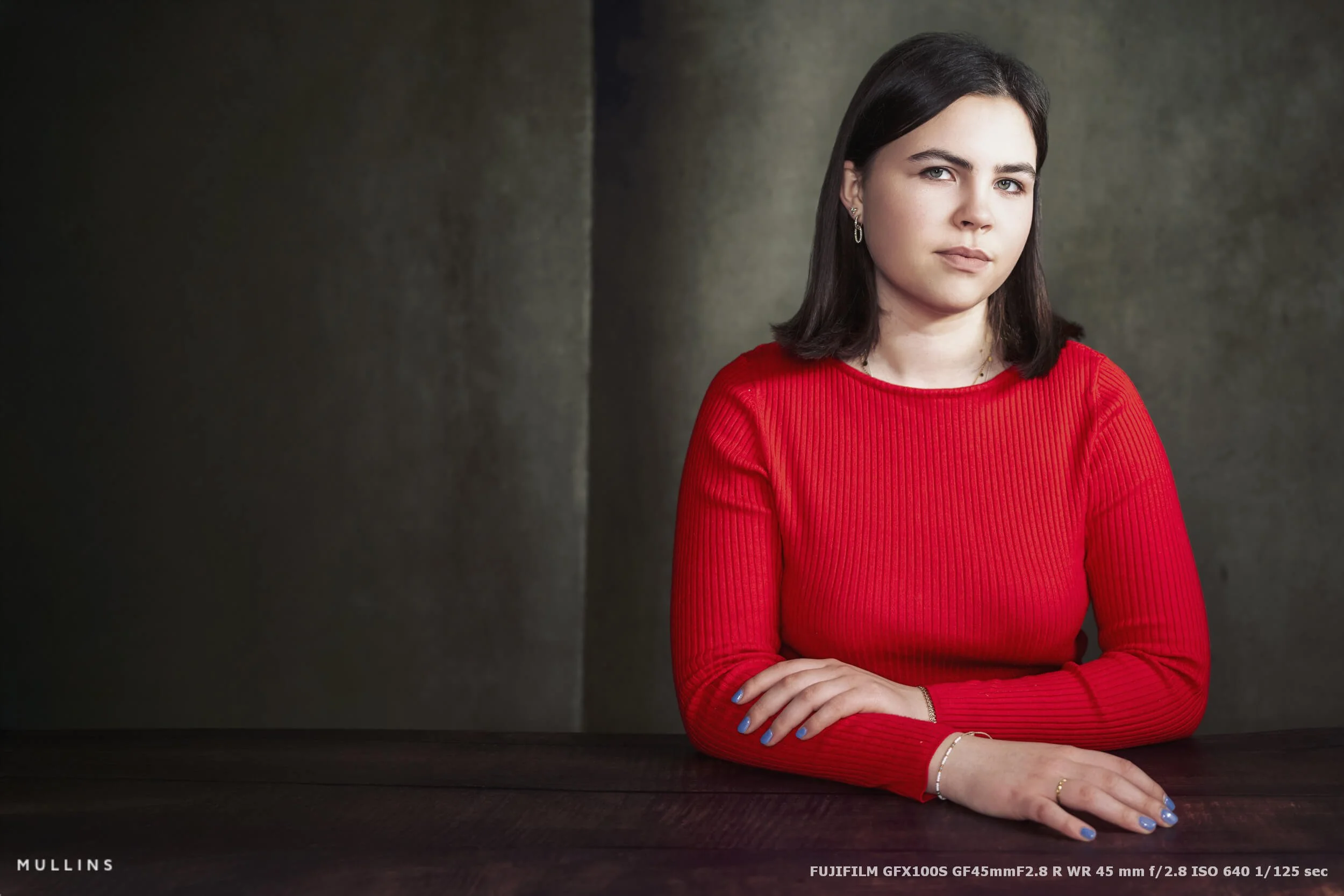 Studio portrait of a young lady sat behind a desk.
