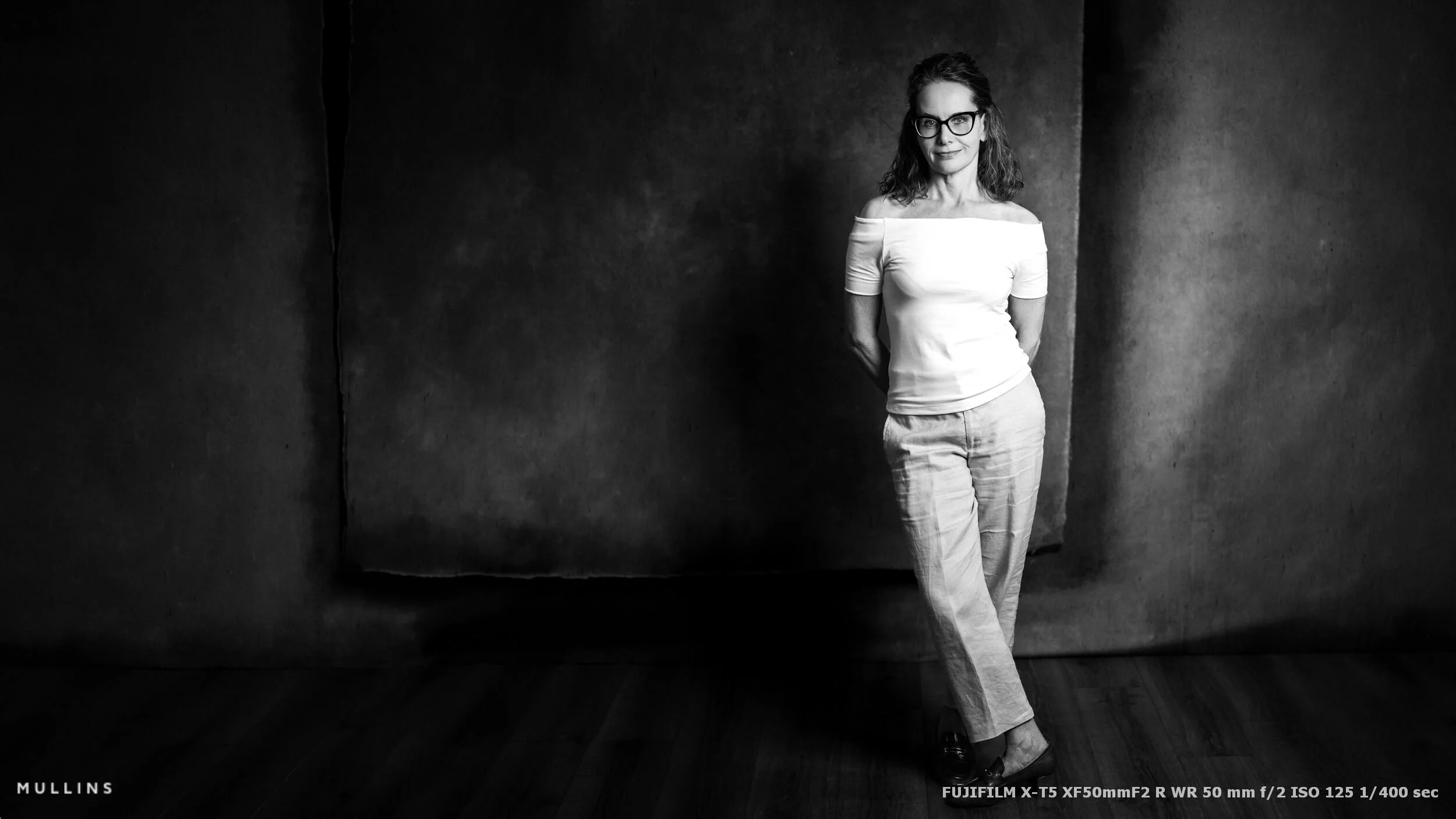 Wide full-length black-and-white actor portrait with the studio backdrop and surrounding space visible