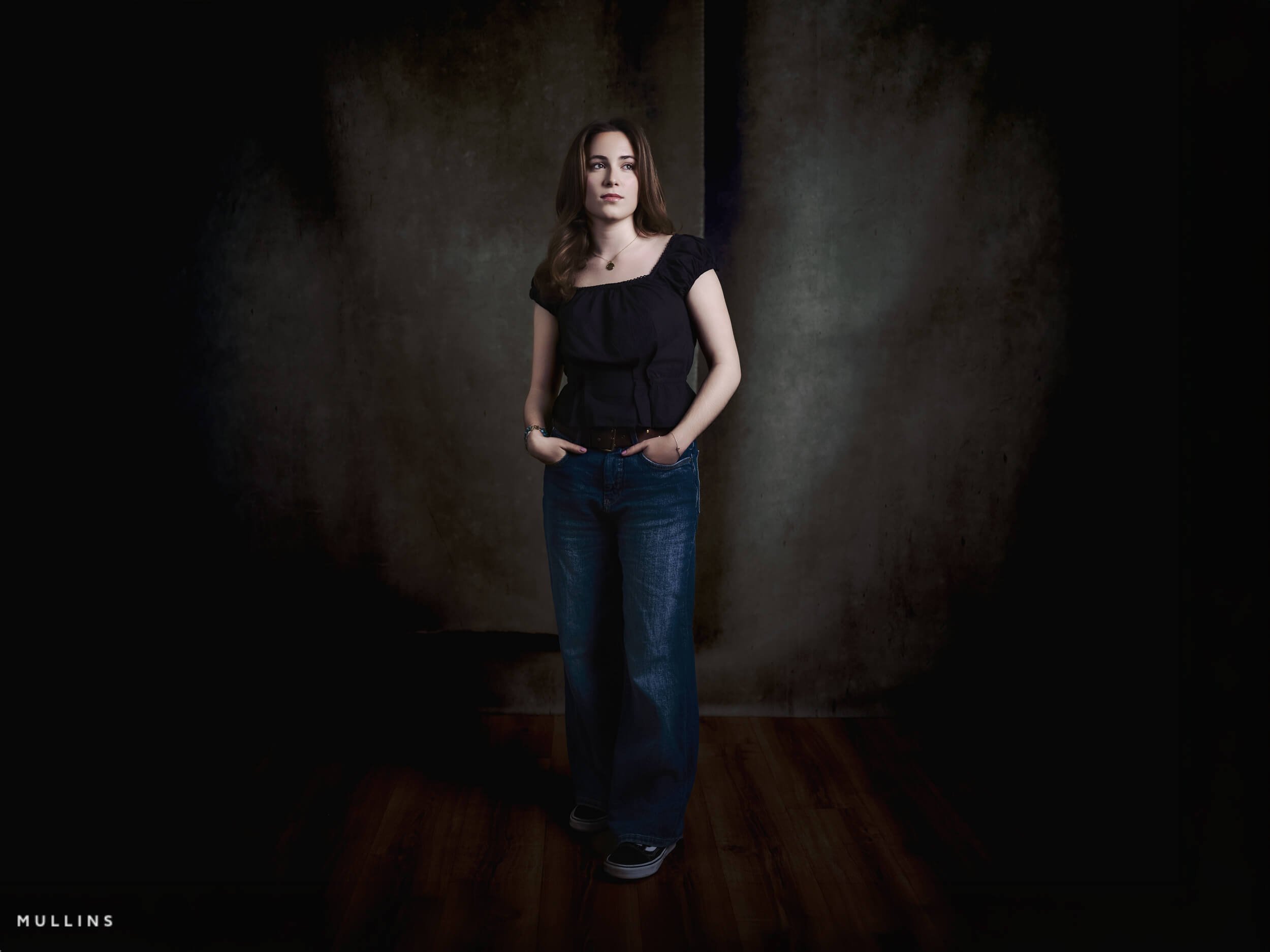 Actor portfolio photo of a young actress seated at a wooden table with books beside her in Kevin Mullins’ Malmesbury studio.