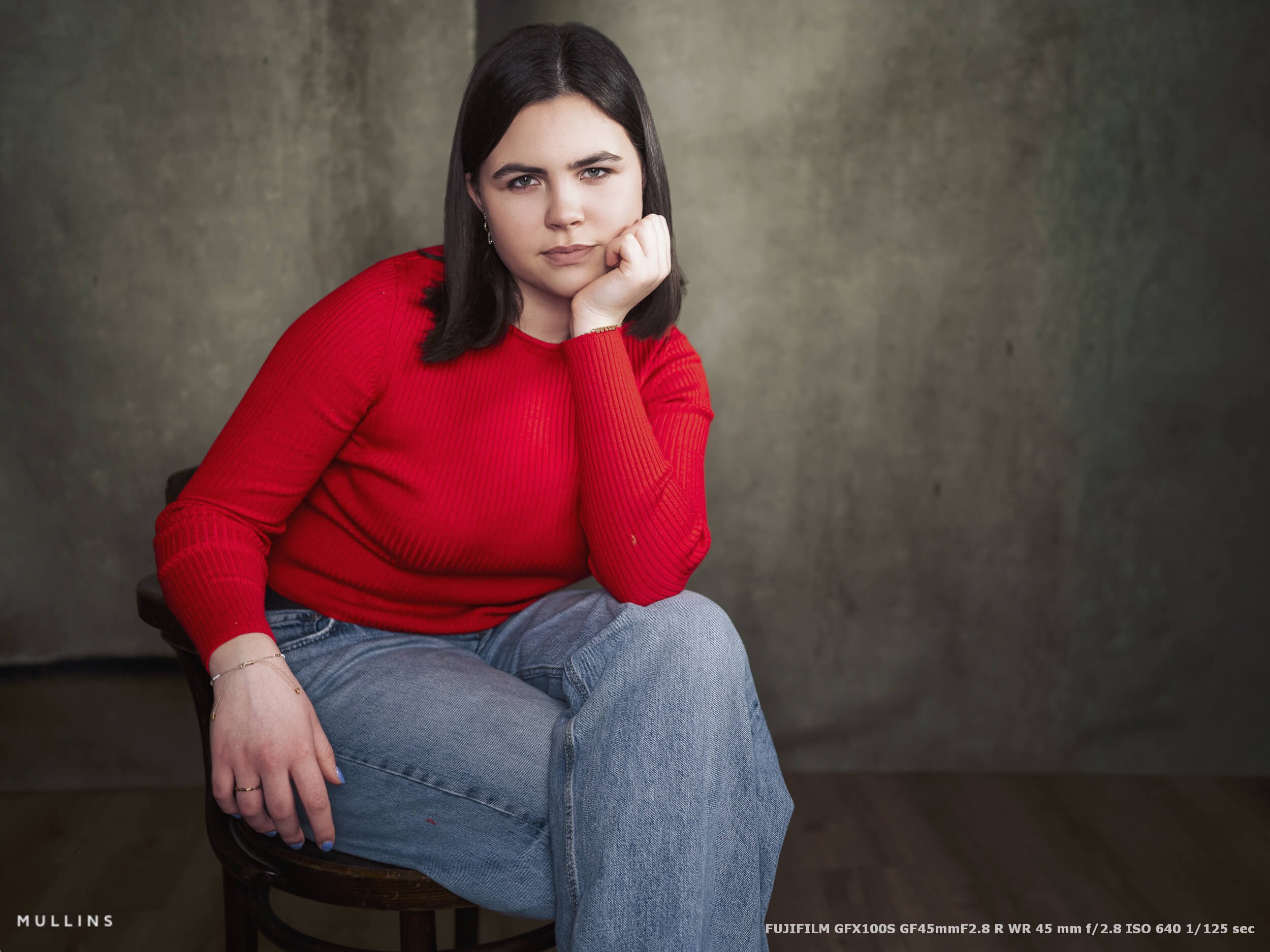 A closer seated portrait of a girl resting her head on one hand, with shallow depth of field and soft studio light, photographed using the GF45mm lens.