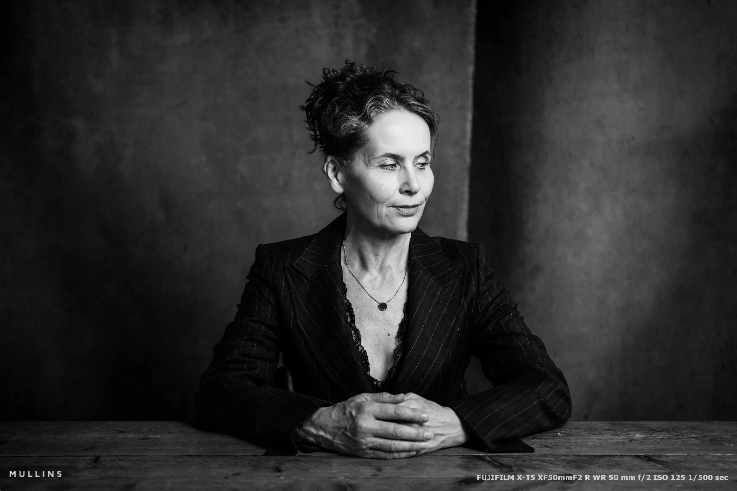 Black-and-white actor portrait seated at a table and looking out of the frame