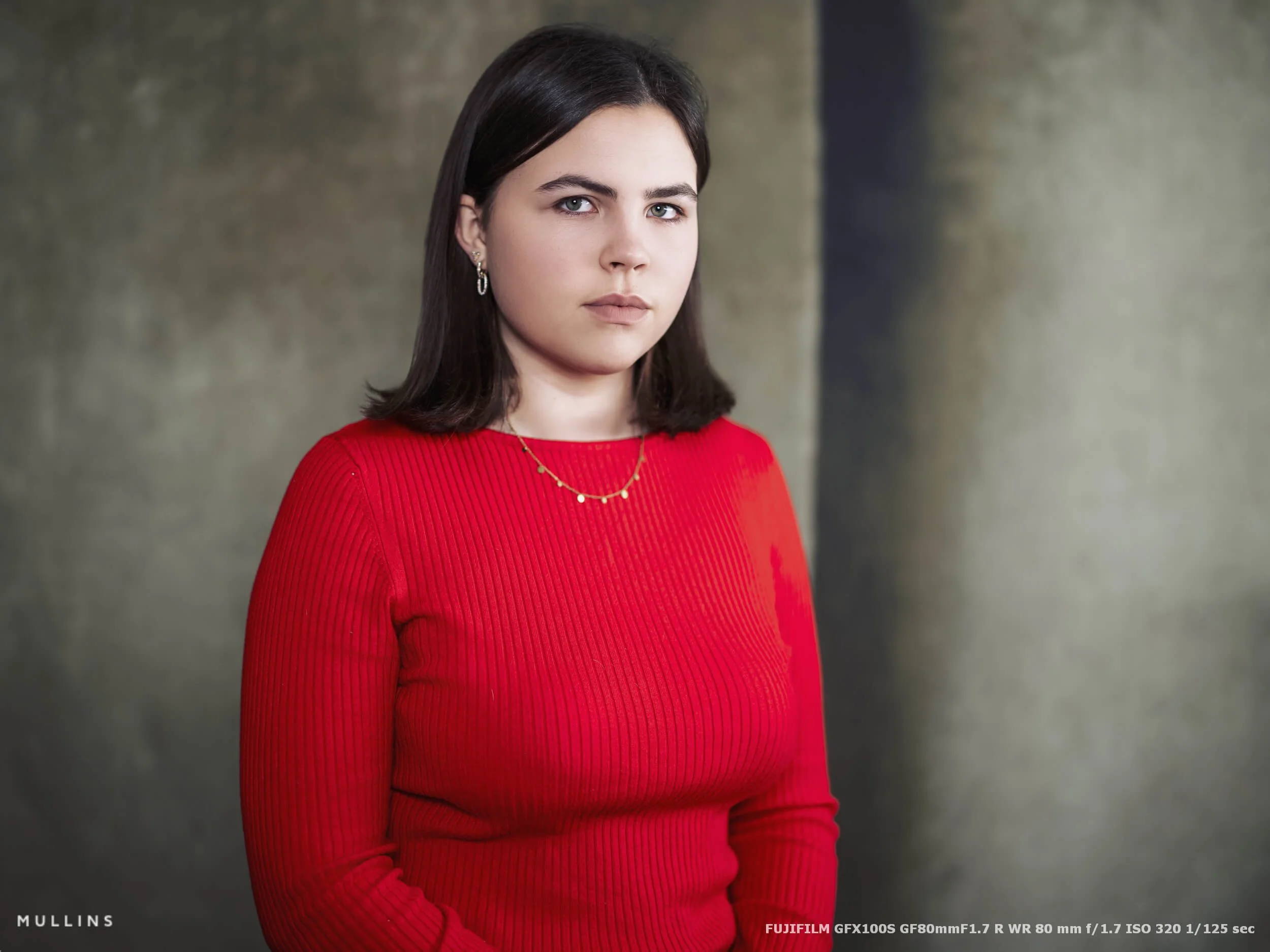A tight portrait of a girl standing against a textured studio backdrop, photographed on Fujifilm GFX100S with GF80mm f/1.7 lens