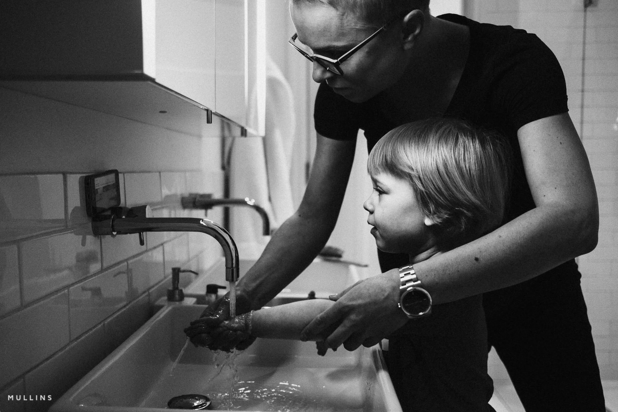 A mother helps her young daughter wash her hands
