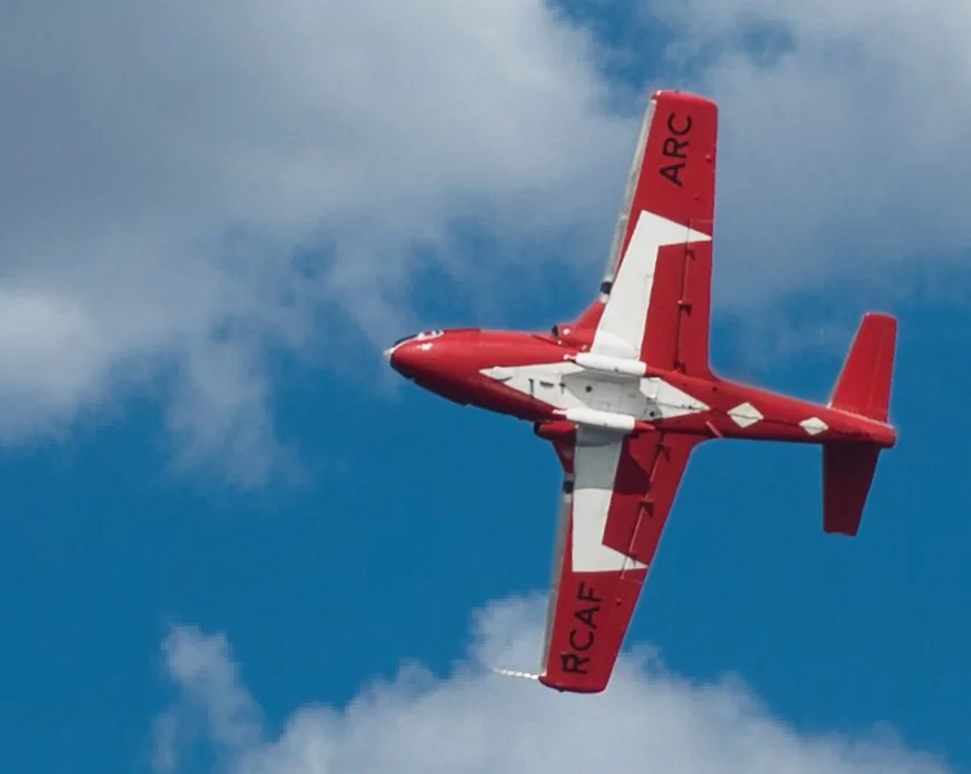 Red and white aerobatic airplane flying in a clear blue sky with some clouds.