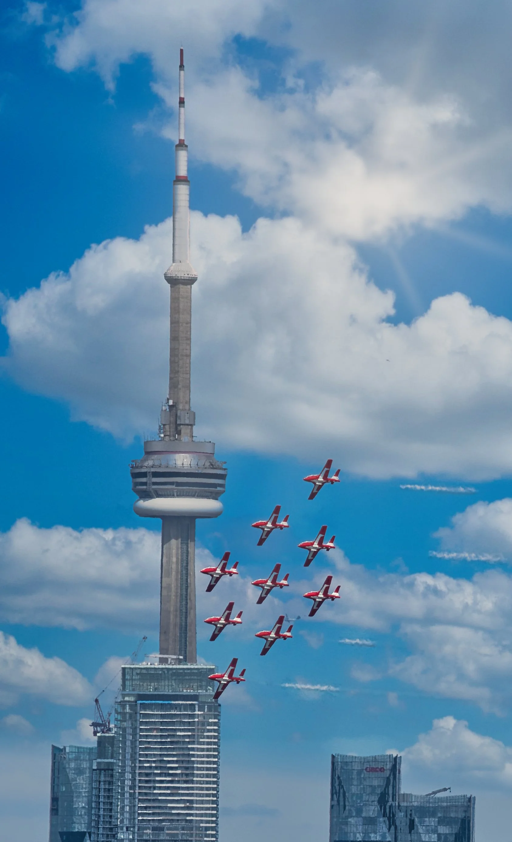 The CN Tower in Toronto with a formation of red and white aircraft flying in the sky.