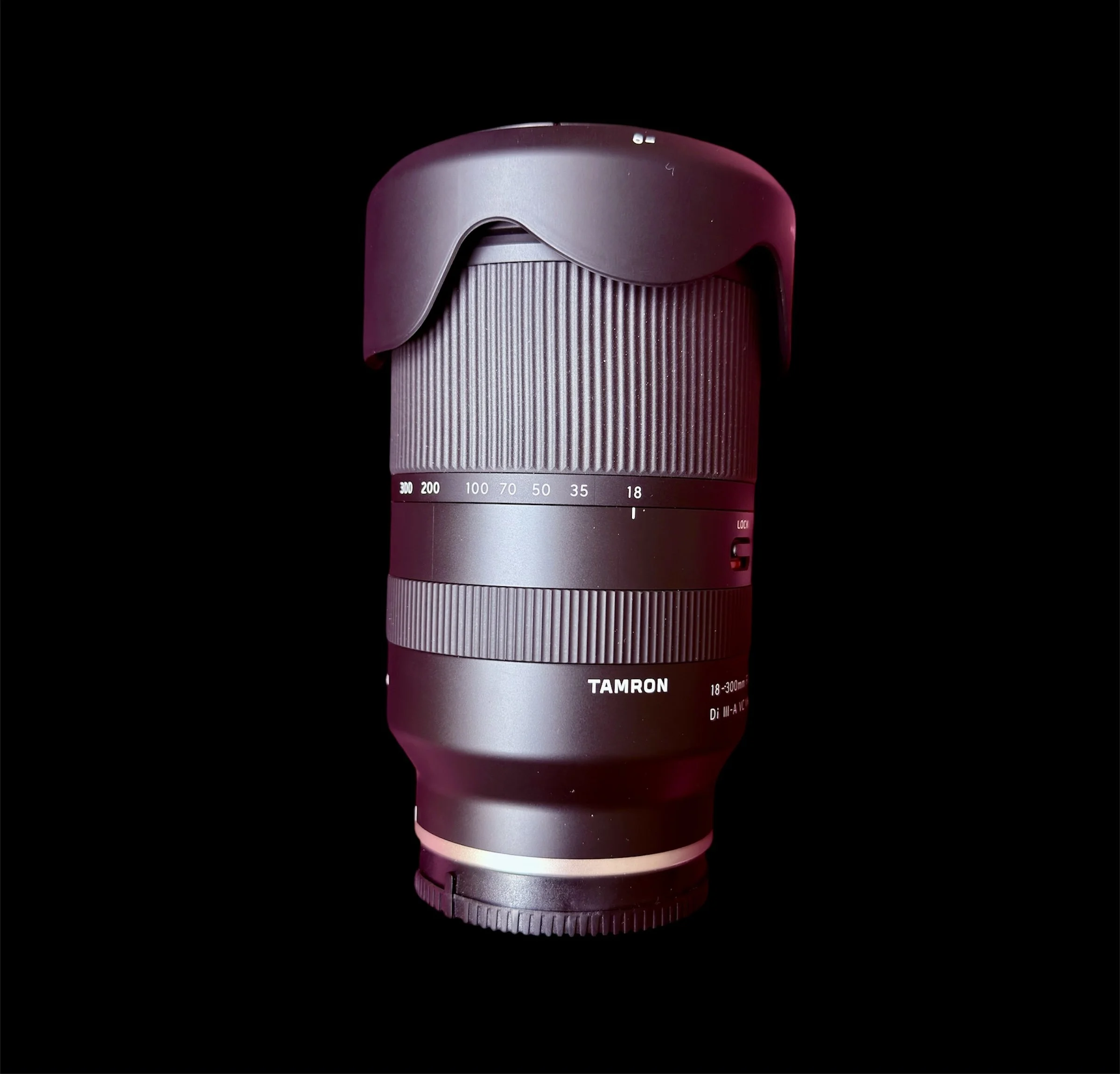 A camera lens with a ribbed grip, labeled Tamron 18-300mm, set against a black background.
